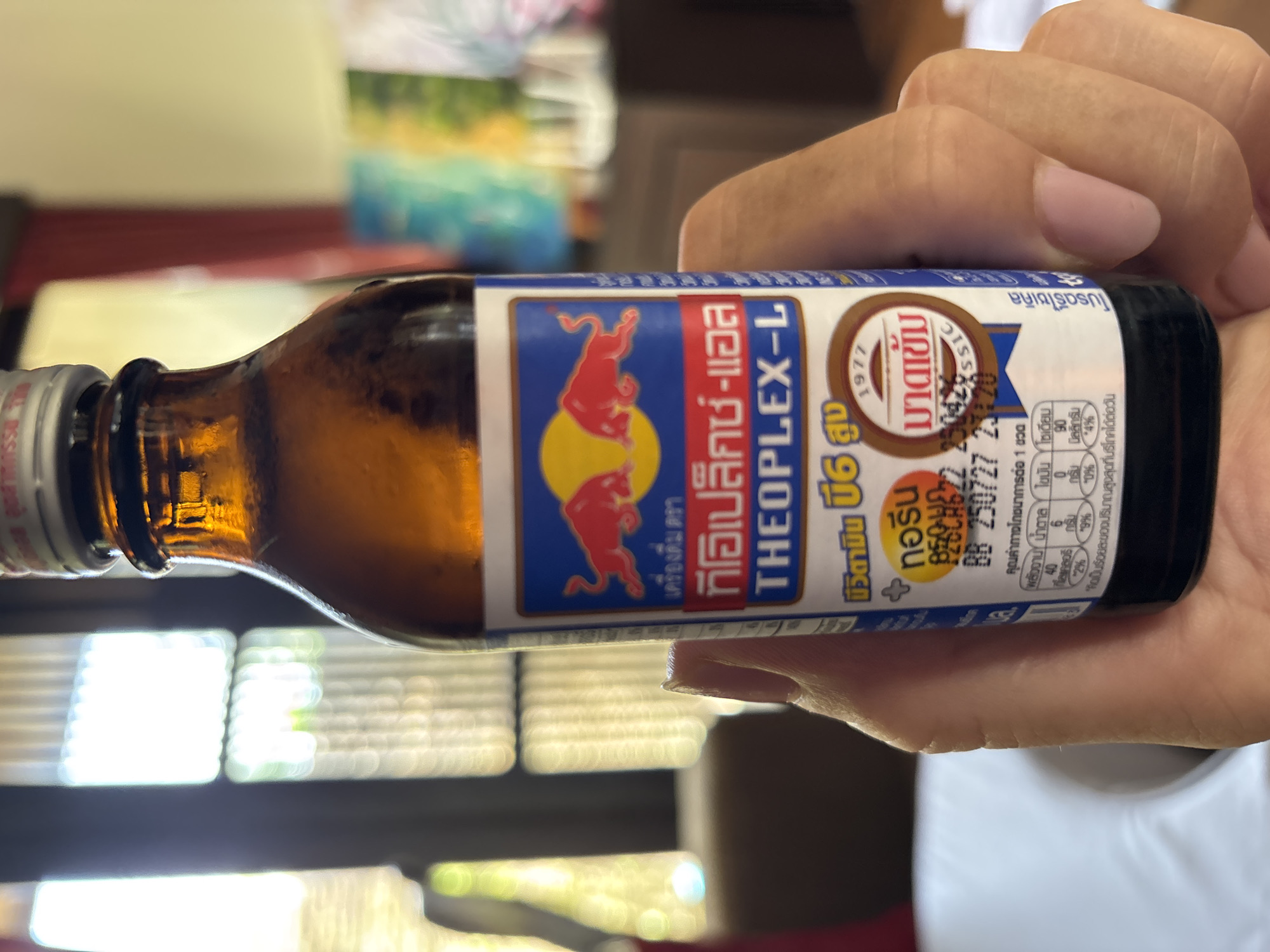 Person holds Thai energy drink with red bulls logo