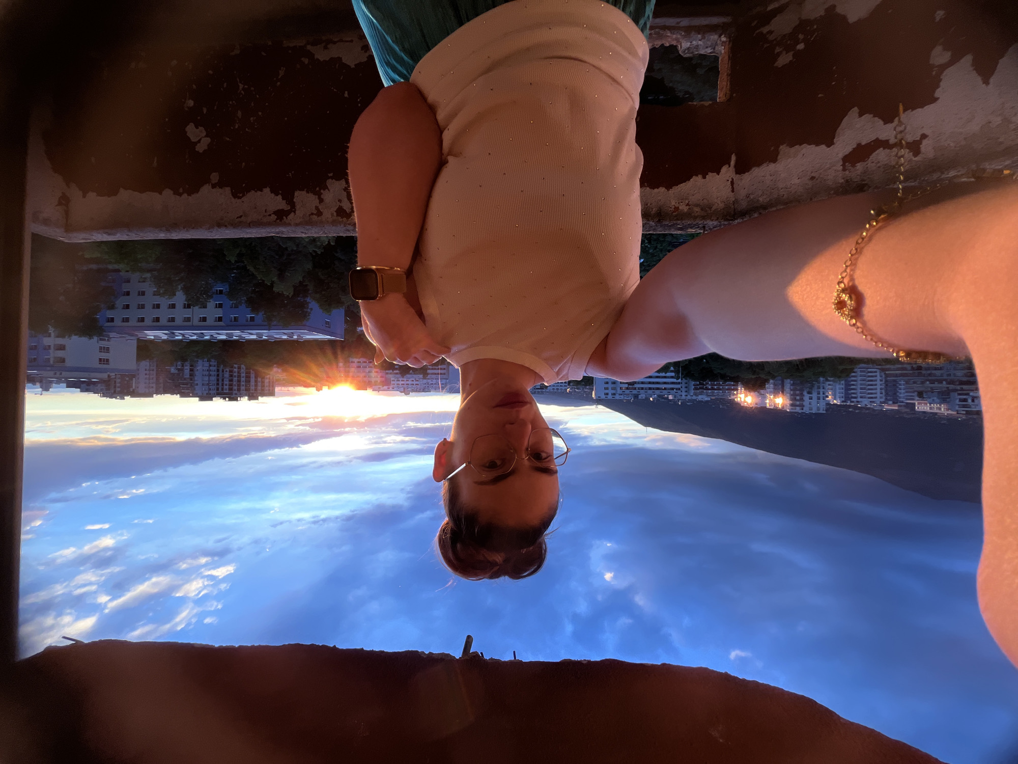 Woman captures sunset selfies from city balcony during golden hour