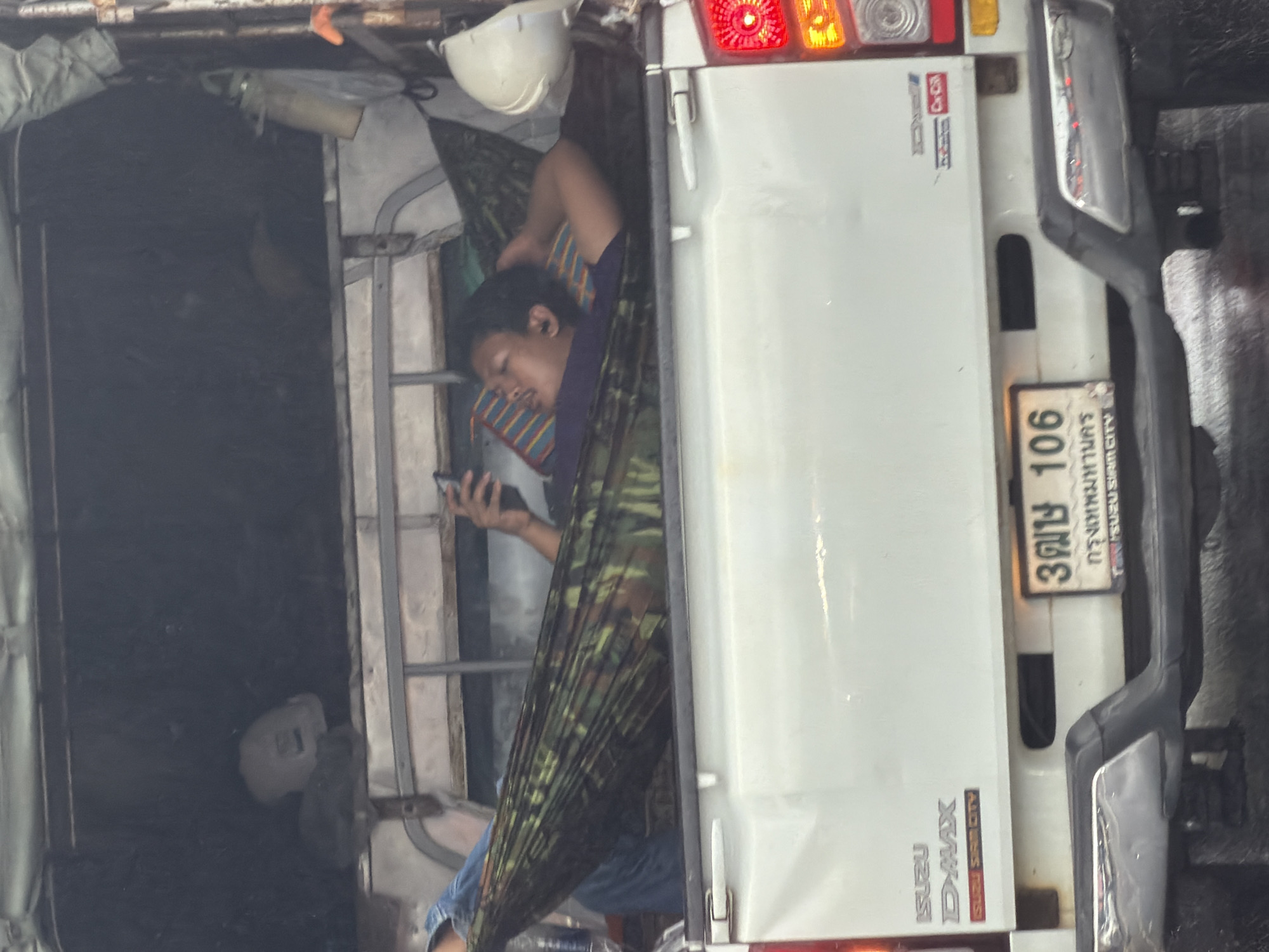 Man relaxes in hammock inside pickup truck bed in Thailand