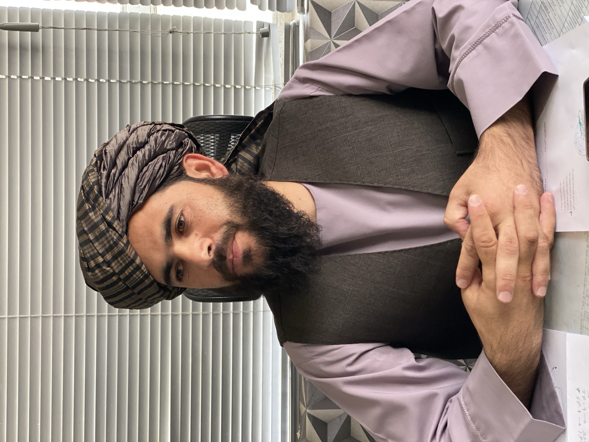 Seated at a desk in Kandahar, hands clasped, formal posture.
