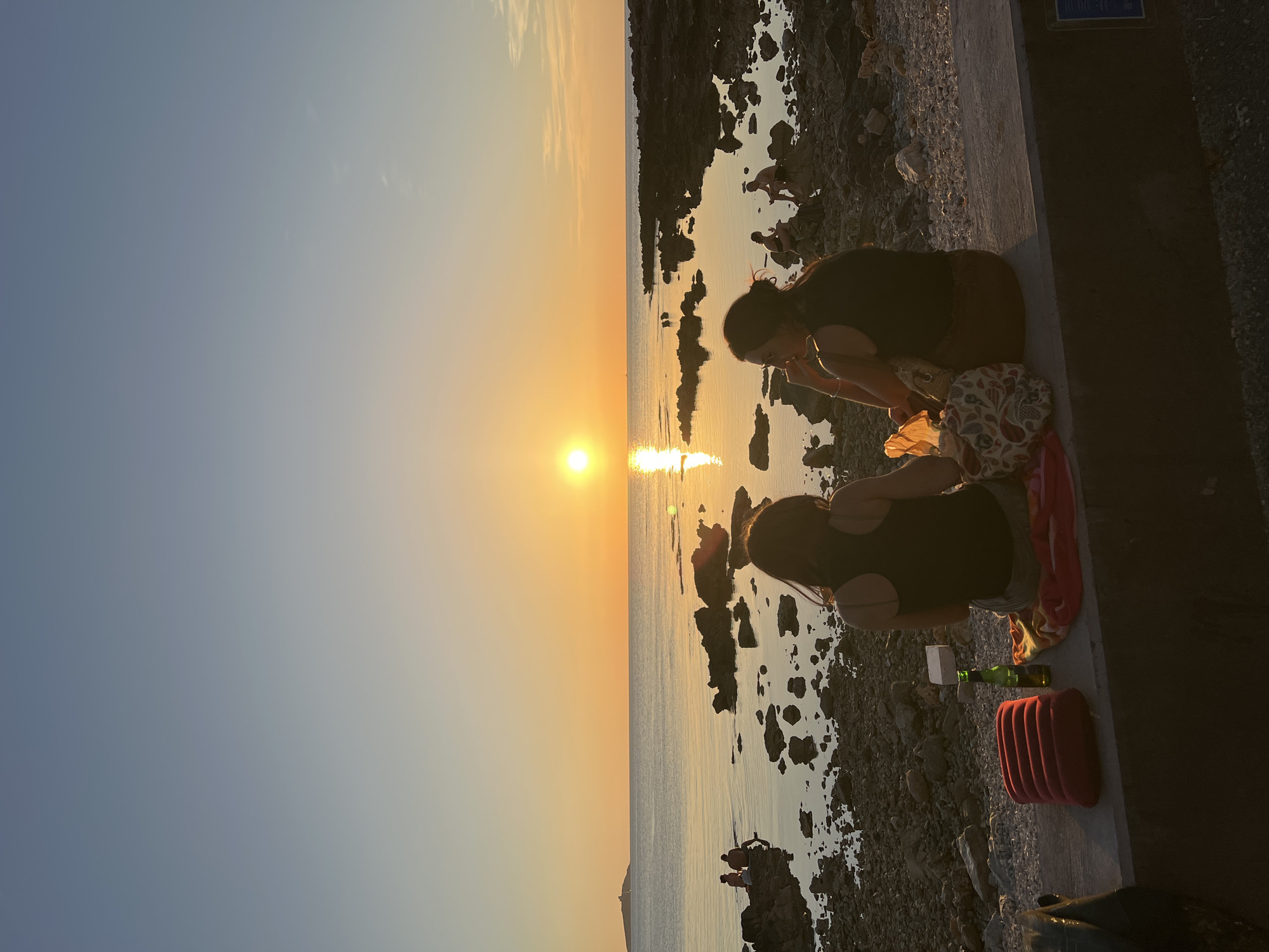 Golden hour on a rocky Palermo coastline, people unwinding at sunset