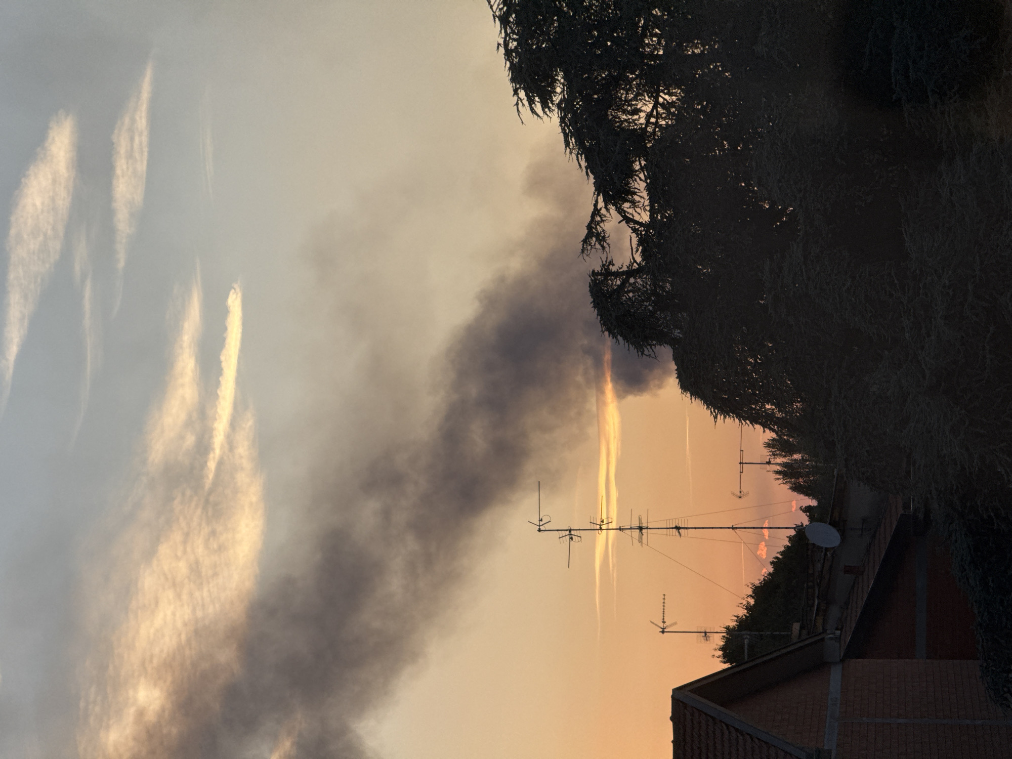 Dark smoke rises over Milan skyline at sunset