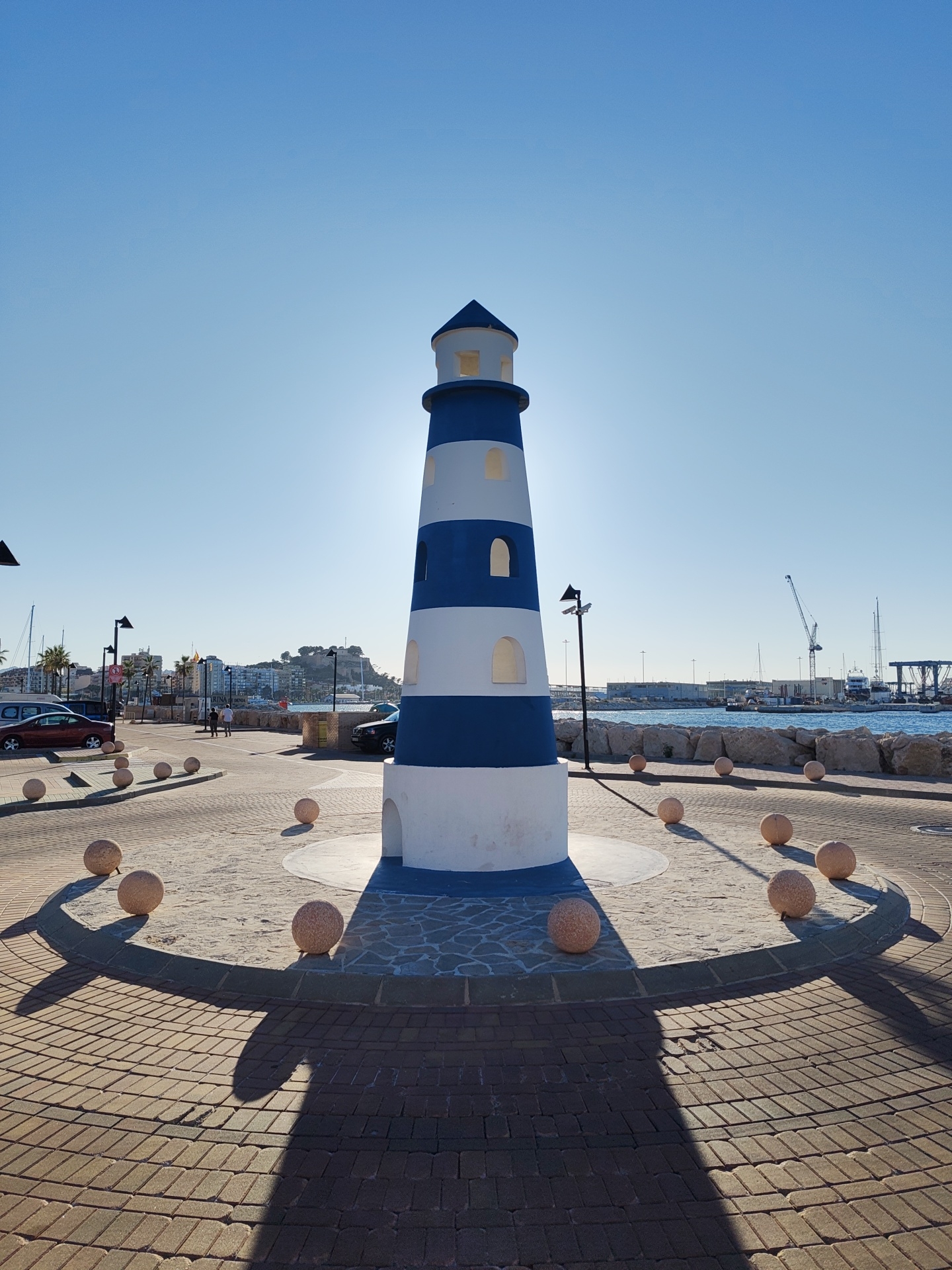 Tourists photograph striped lighthouse monument in Dénia harbor