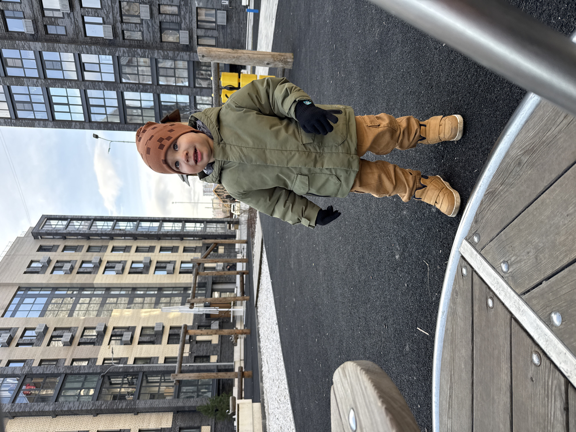 Toddler in winter clothing stands on playground surface near building