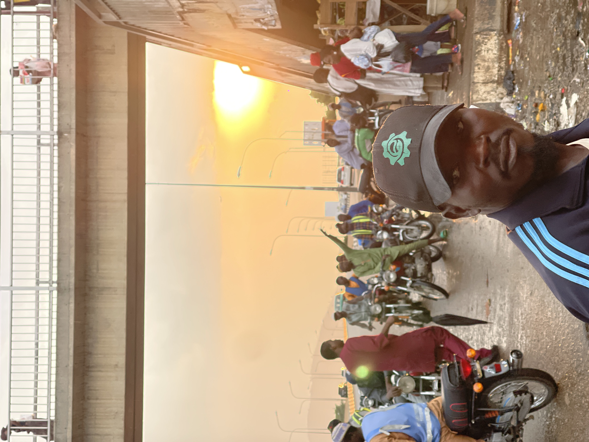 Man poses near motorcycles on busy Gwarinpa street at sunset