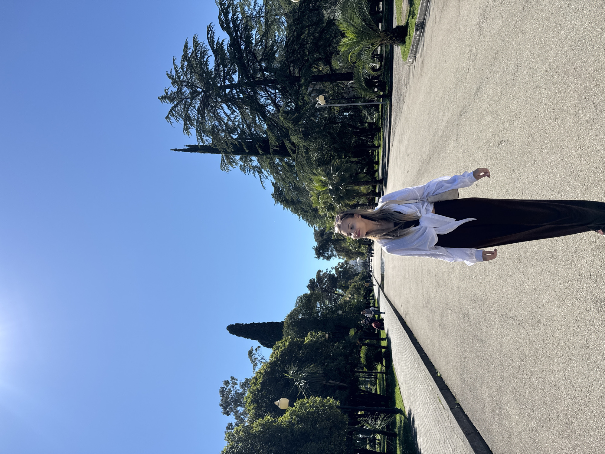 Woman walks tree-lined pathway in Sokhumi under clear skies