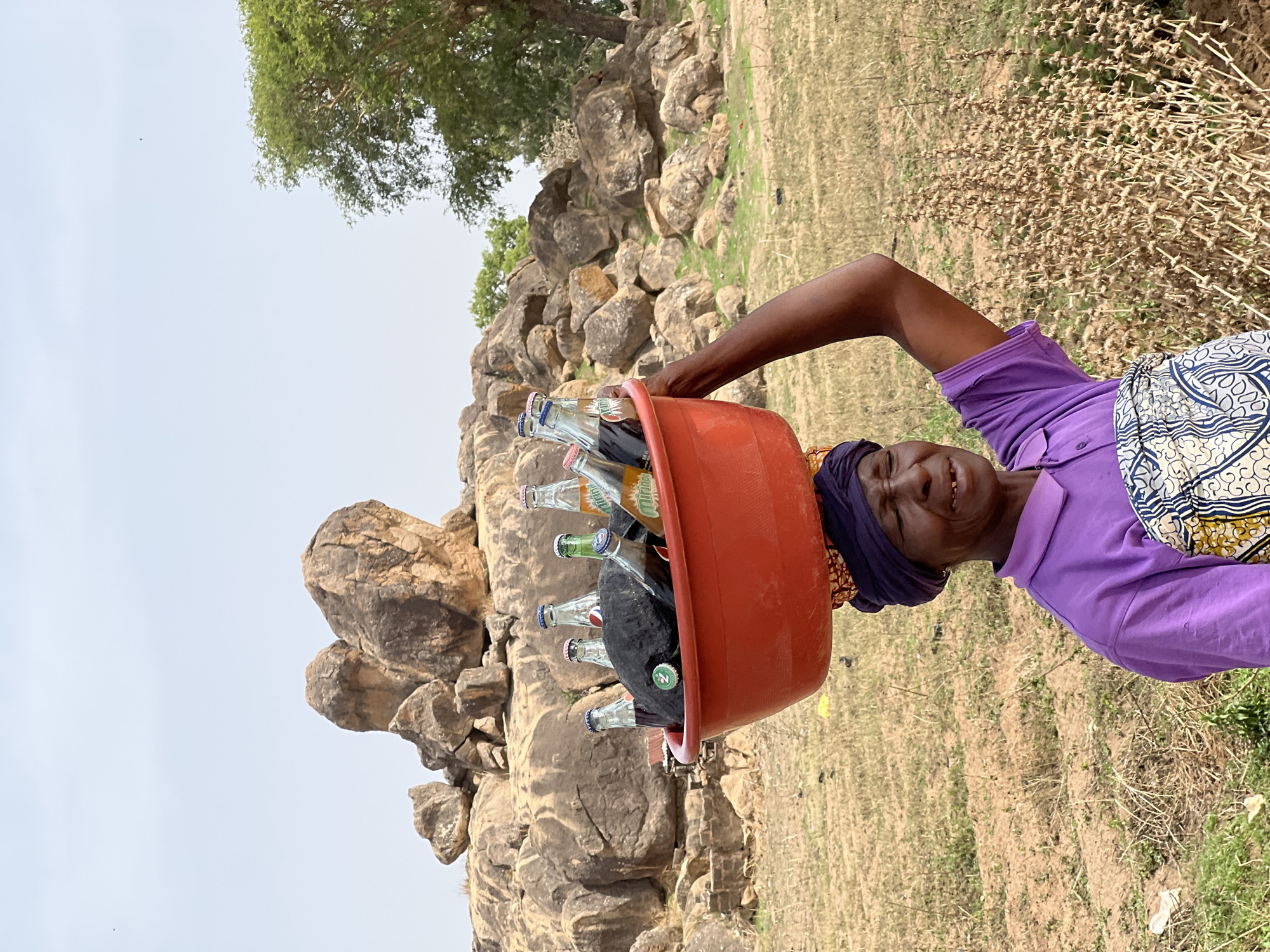 Woman carries bottles in tub on head in Udu