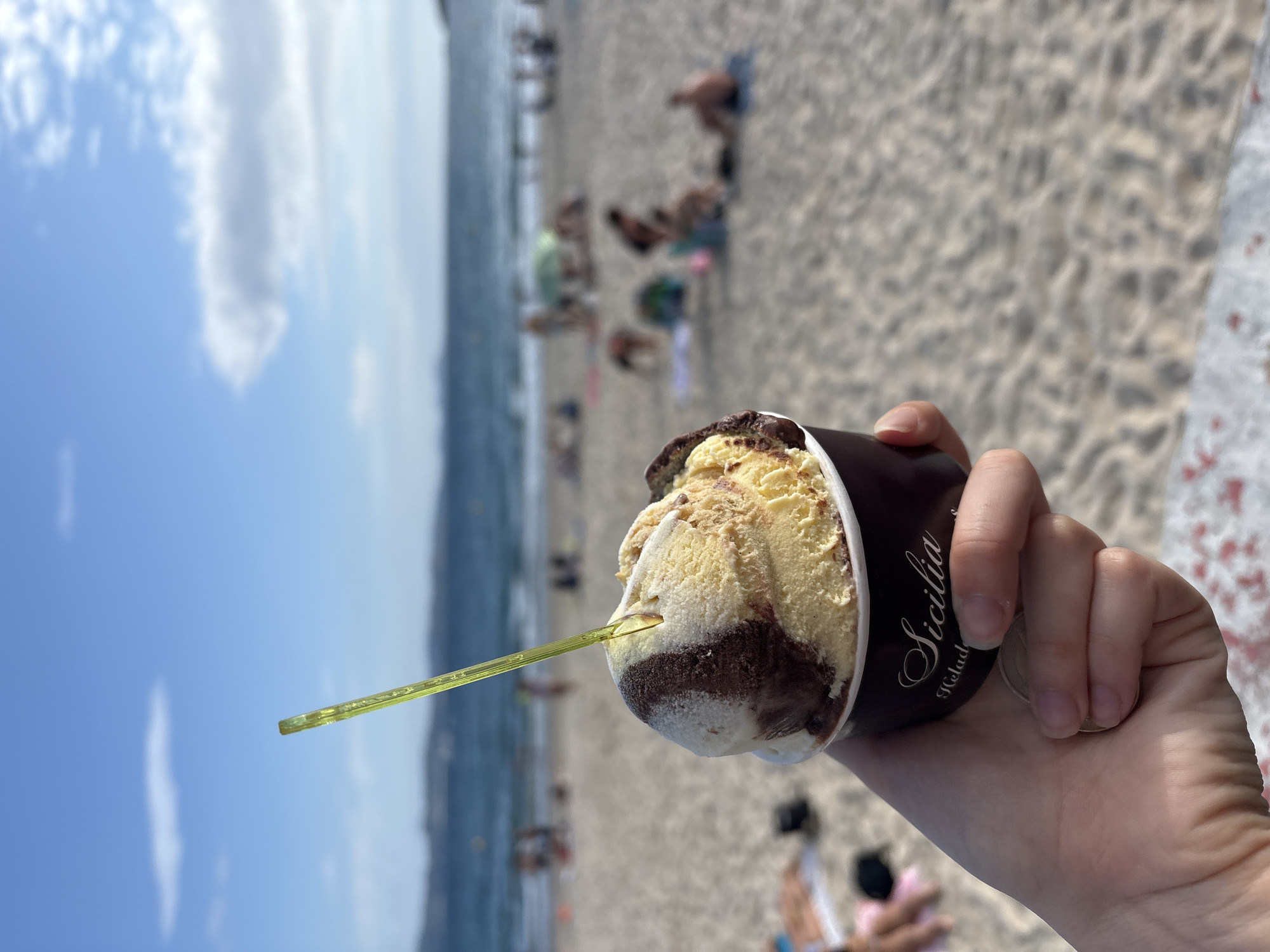 Gelato cup held up against a Sanxenxo beach backdrop
