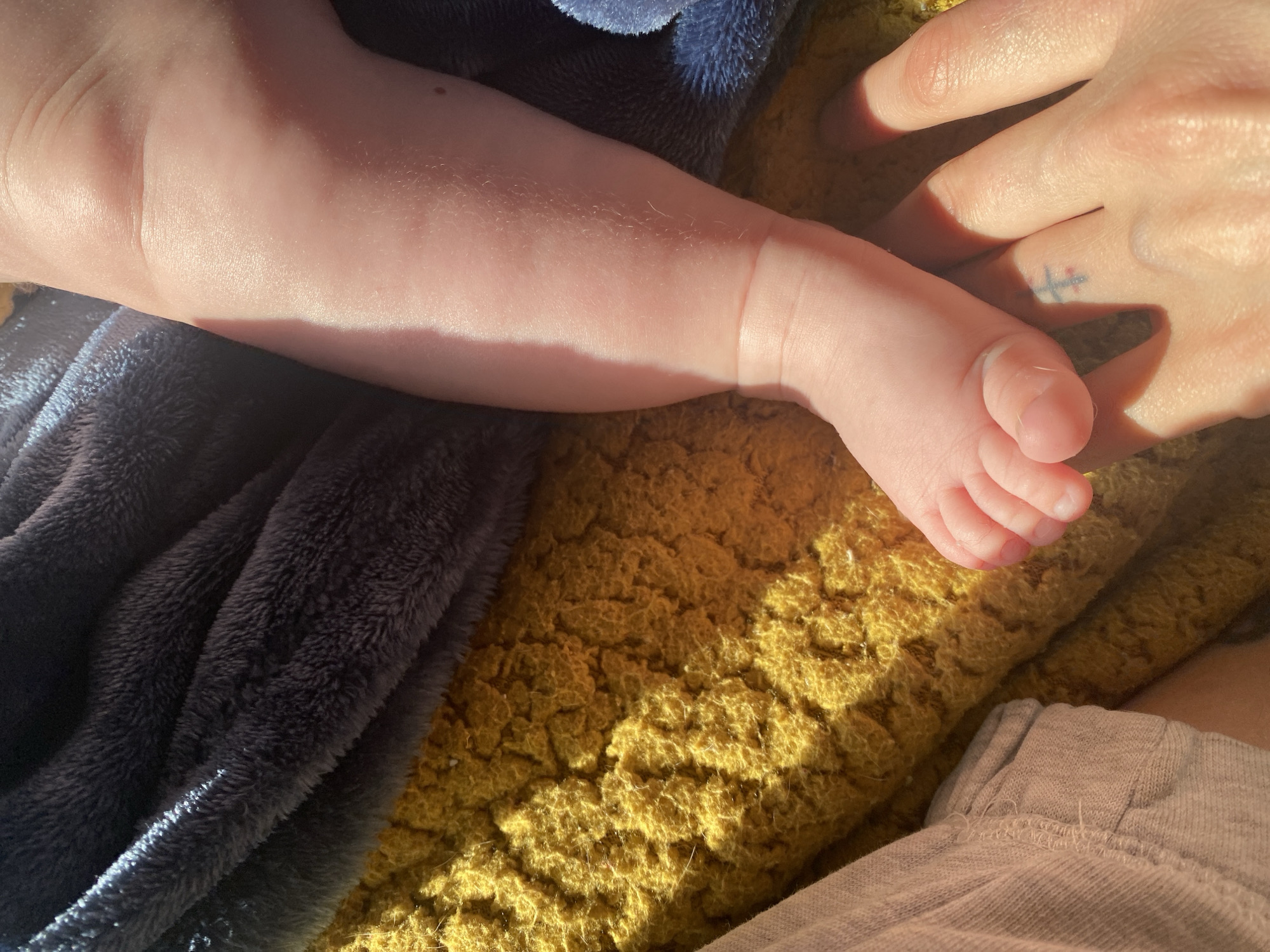 Baby's foot photographed beside tattooed adult hand in Bulgaria