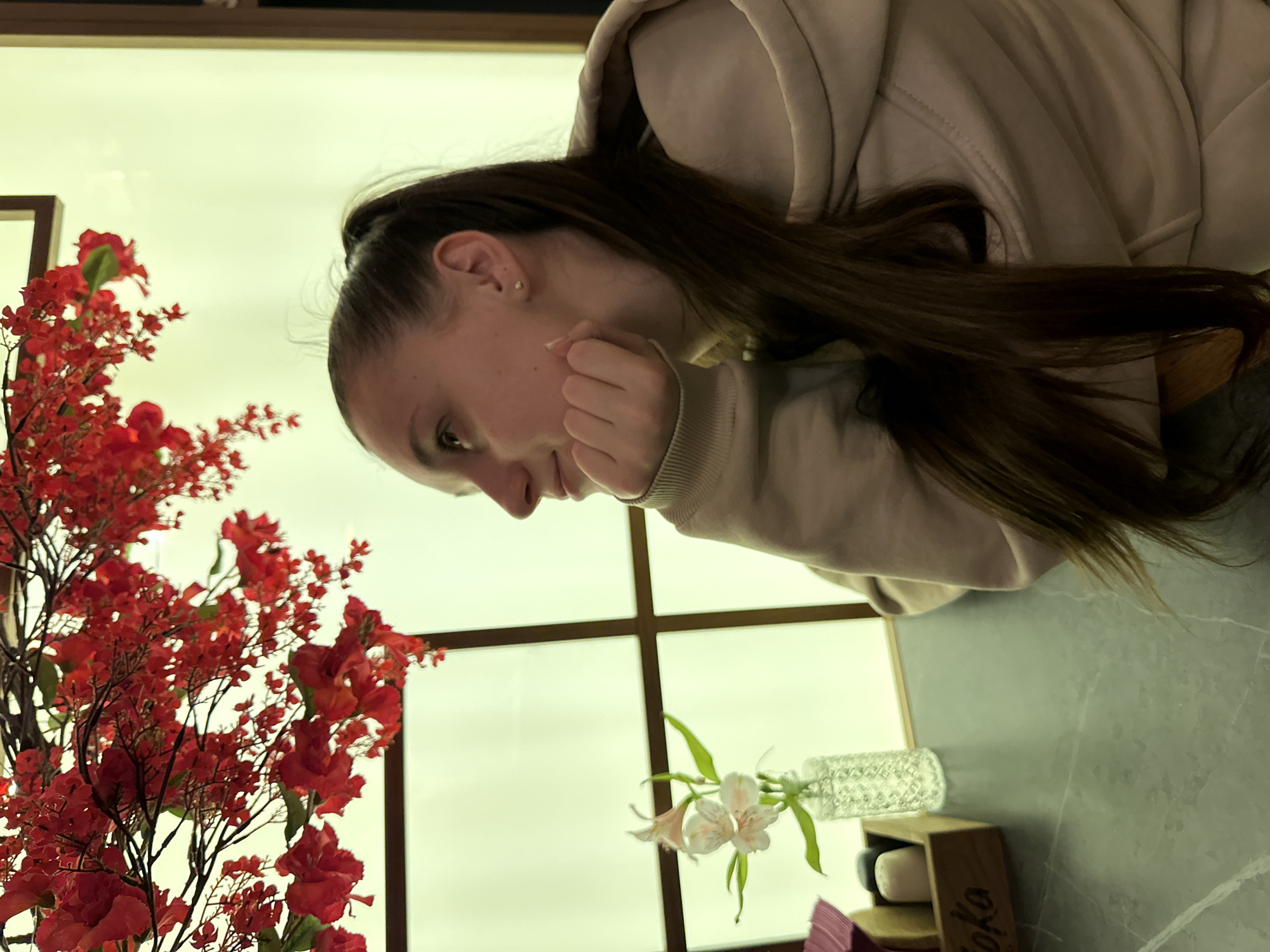 Woman in beige hoodie rests contemplatively at indoor table
