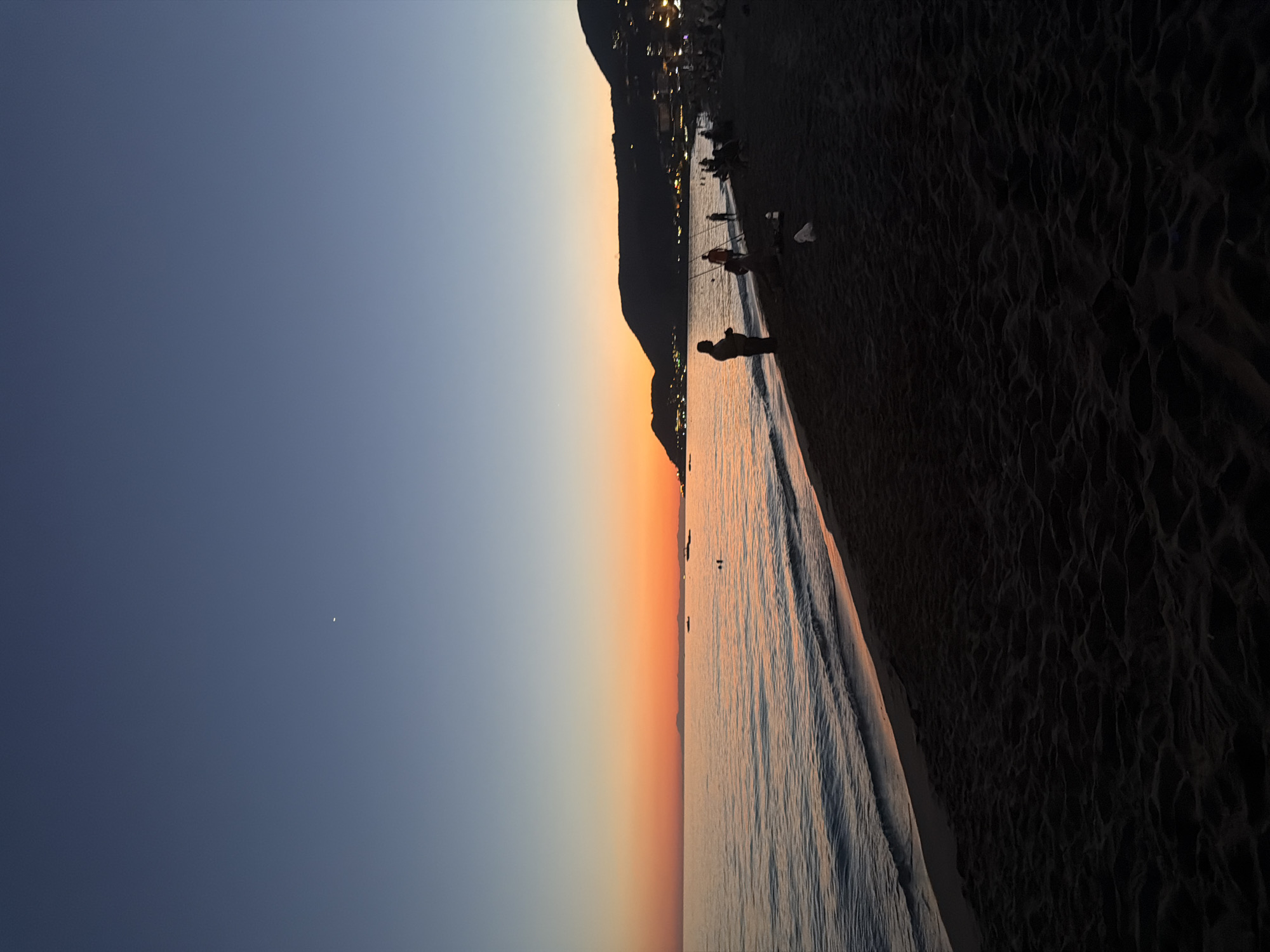 Dusk at the beach: sunset fades, moon rises, town lights appear