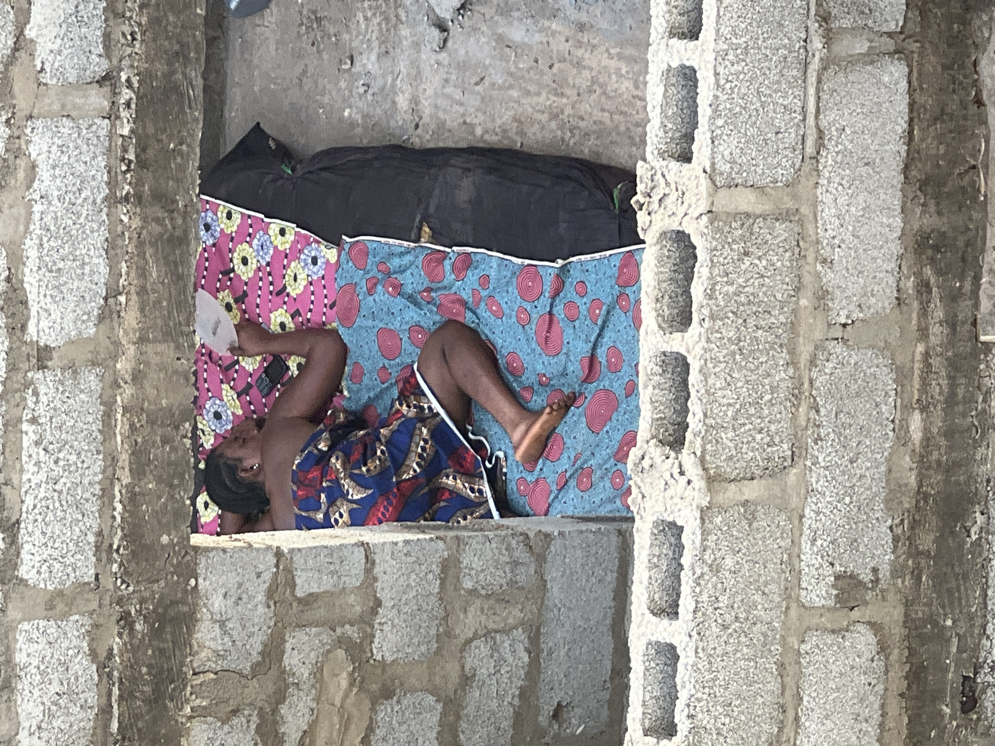 Person rests on bedroll in concrete structure, Abuja
