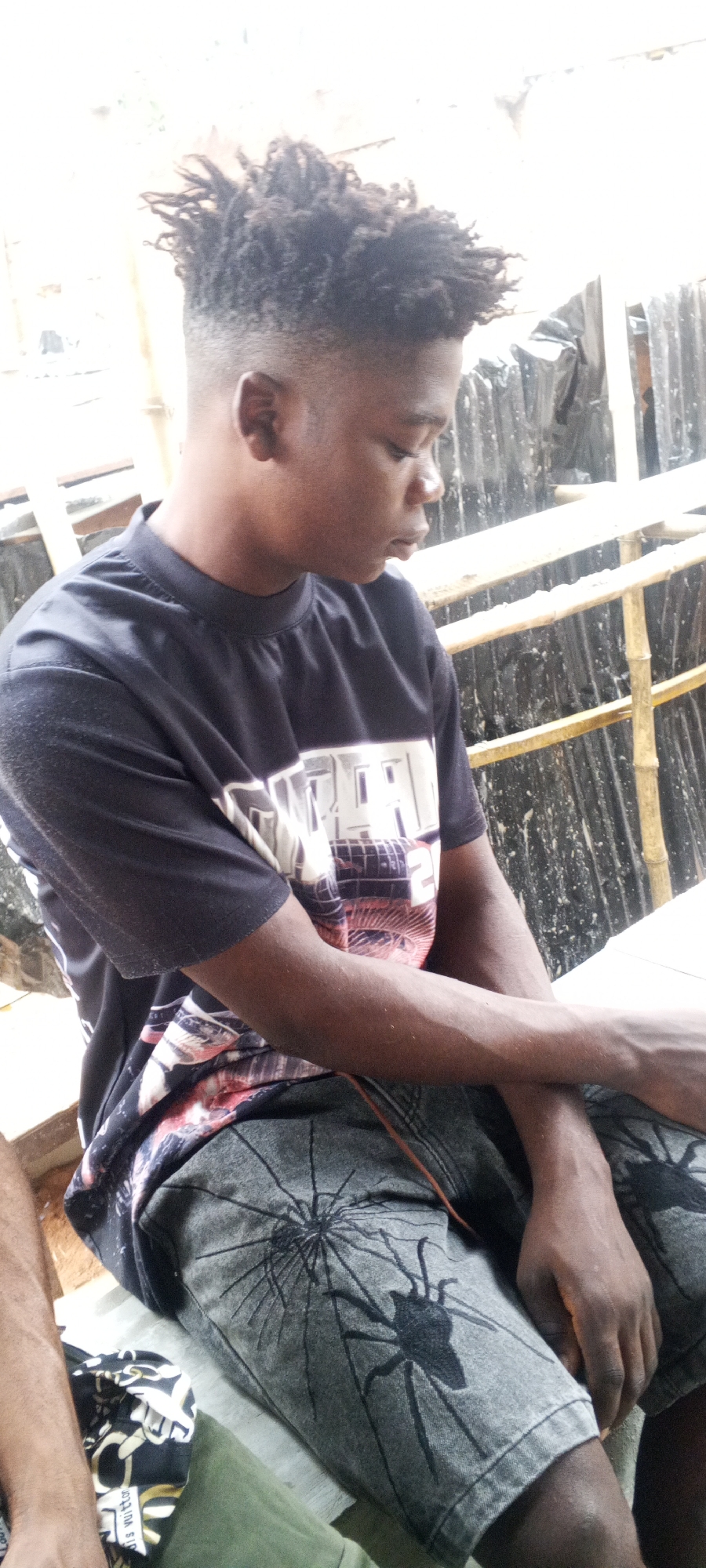 Young man sits quietly in patterned shirt, grey shorts