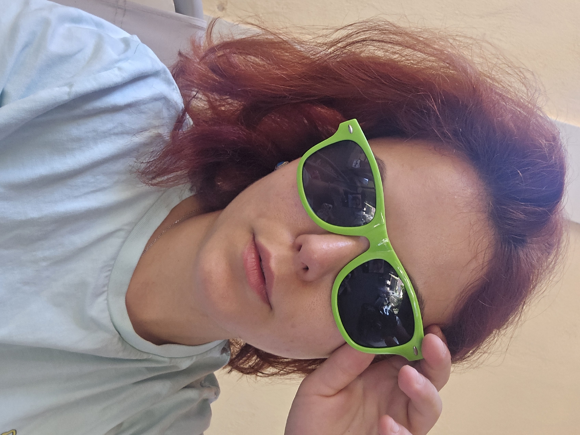Casual indoor portrait, green sunglasses and light blue tee
