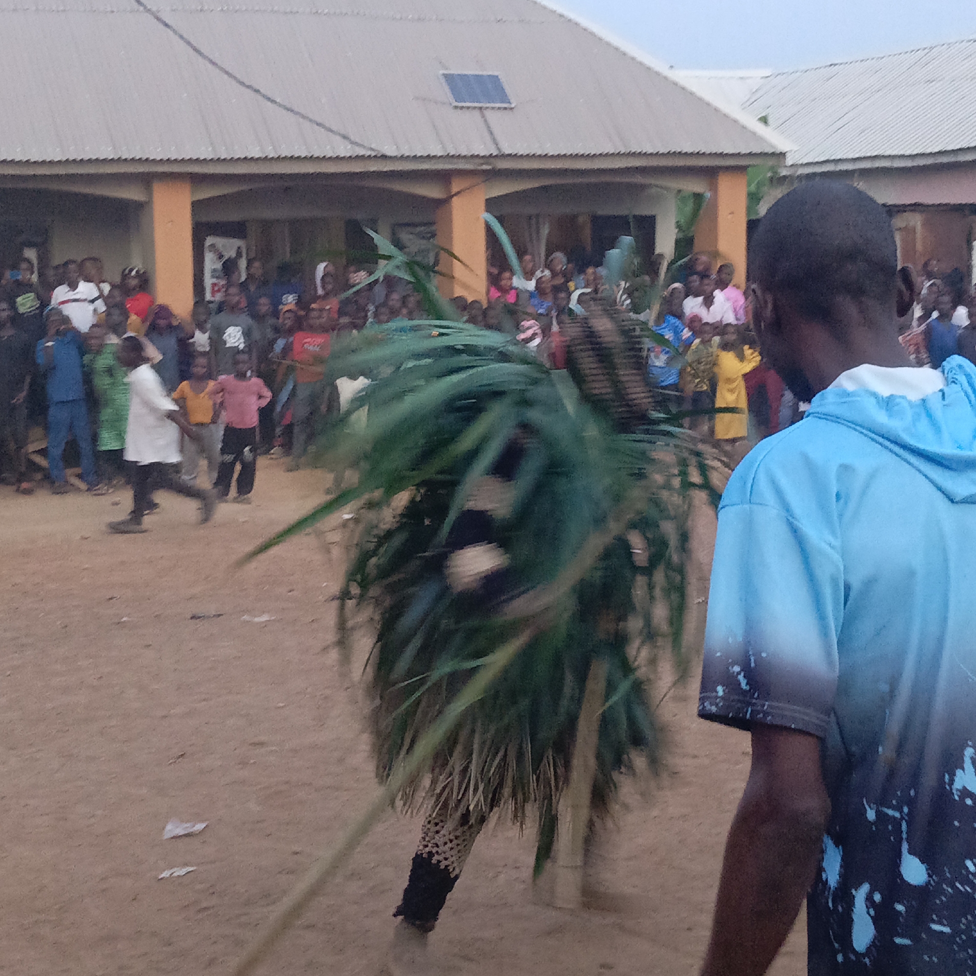 Masked dancers perform with staffs for gathered crowd