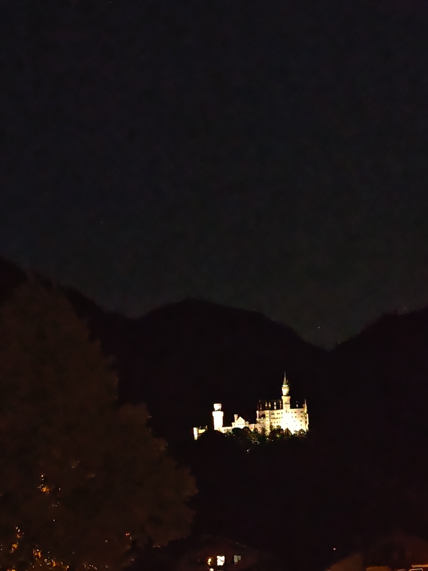 Neuschwanstein Castle glowing against dark mountain silhouettes at night