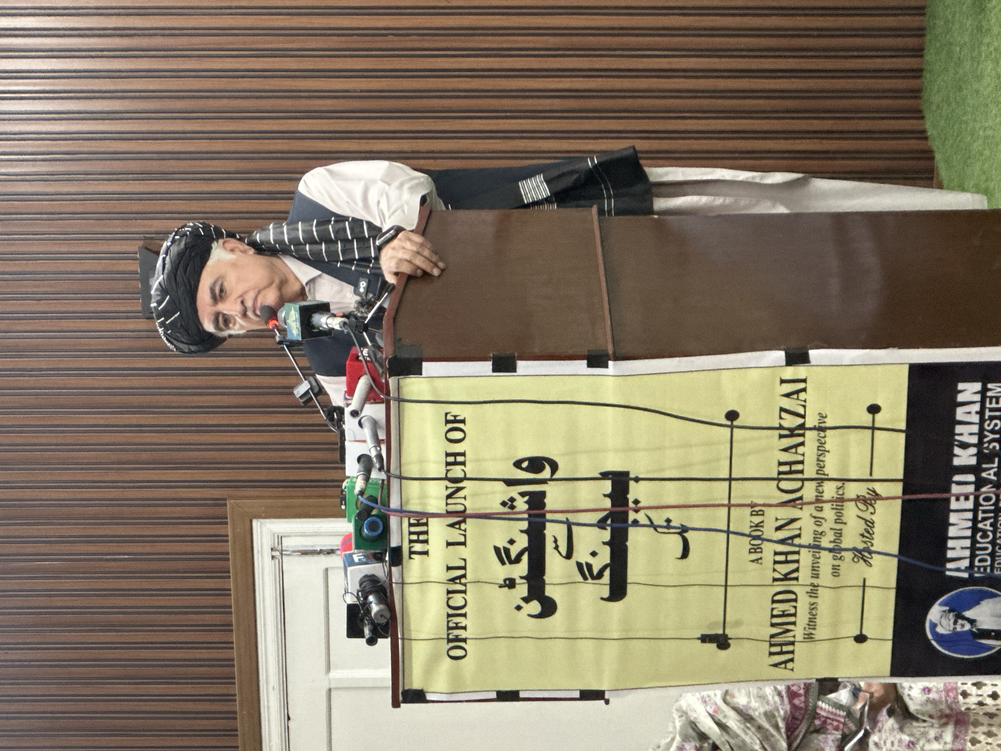 Speaker addresses seated crowd at a formal indoor gathering