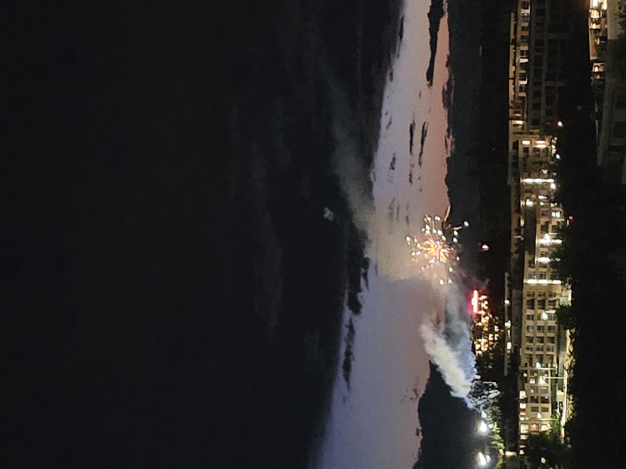 Nighttime fireworks display illuminates unknown city skyline over water