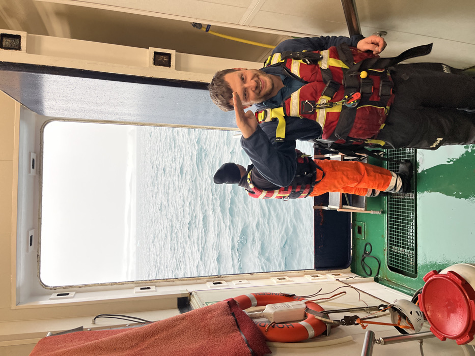 Maritime crew boards vessel in survival gear during snowstorm