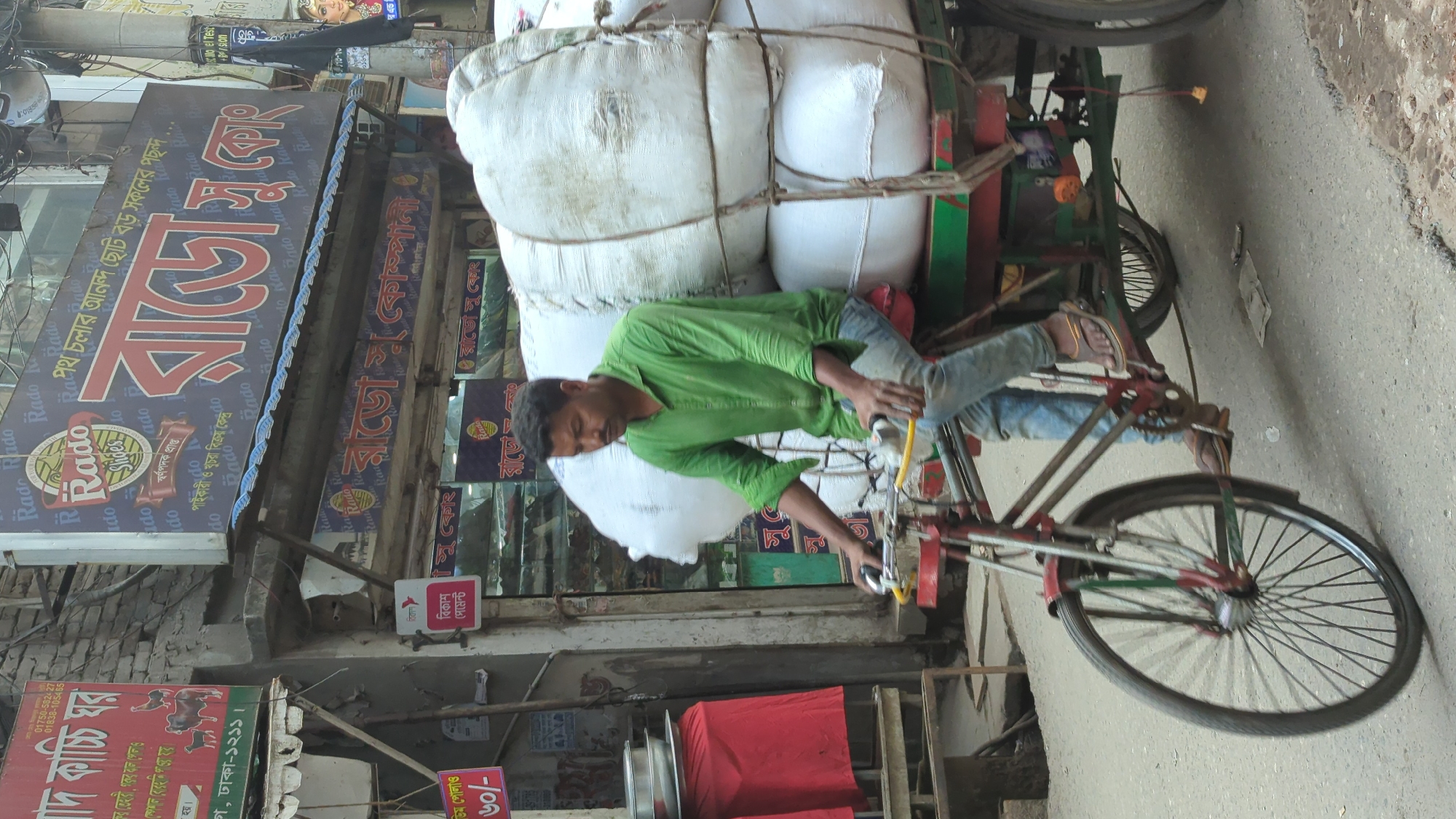 Overloaded rickshaw carries white sacks through Dhaka street