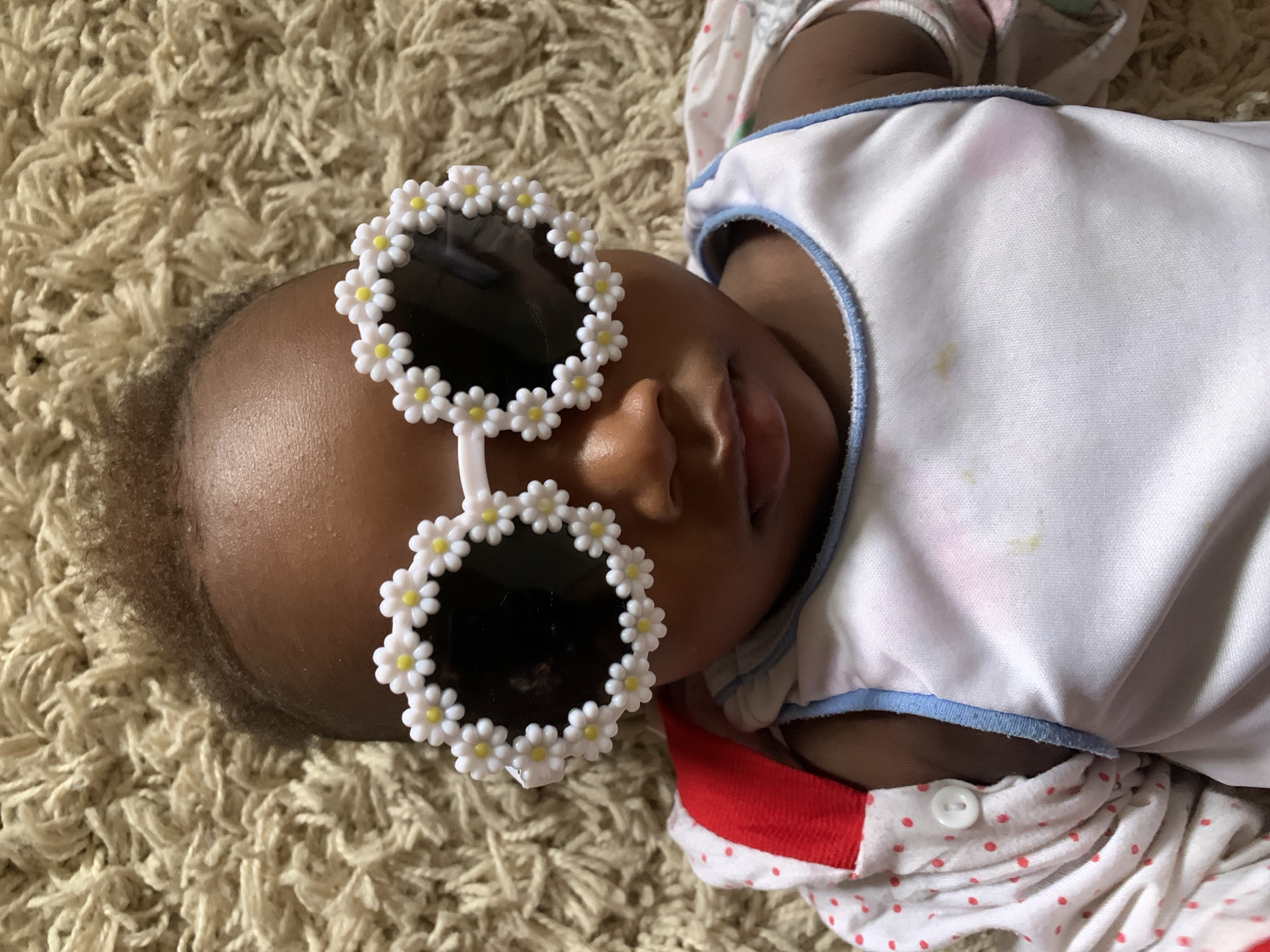 Baby in flower sunglasses photographed on carpet in Nigeria