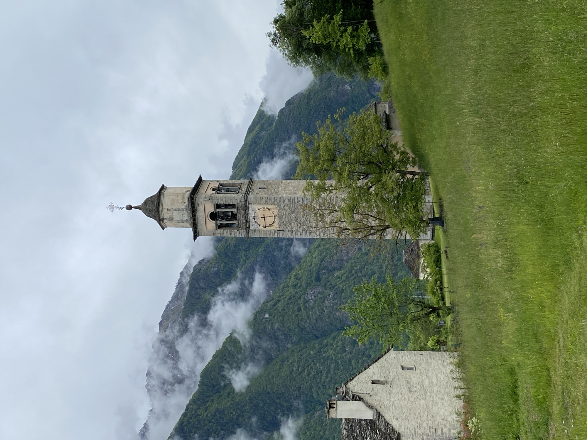 Church tower observed amid foggy mountains in Crodo, Italy