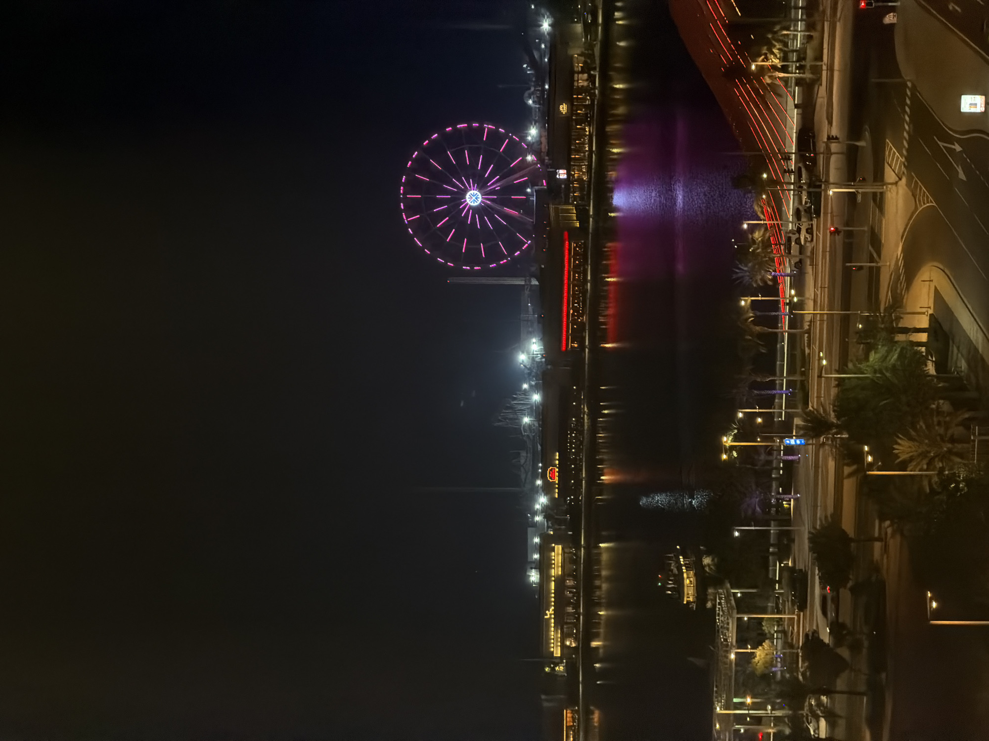 Ferris wheel and crescent moon over a lit Gulf waterfront