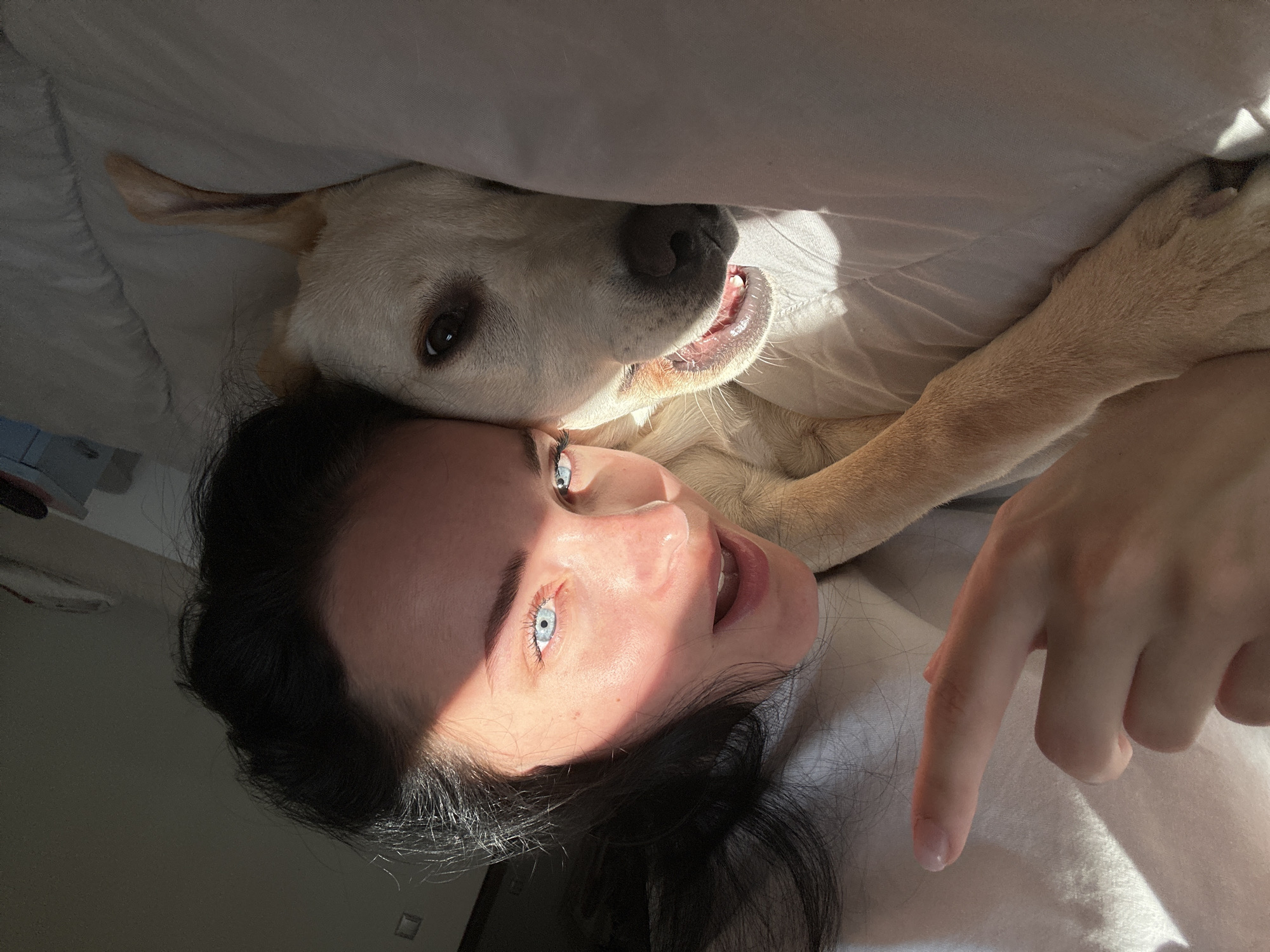 Woman rests in bed with light-colored dog companion
