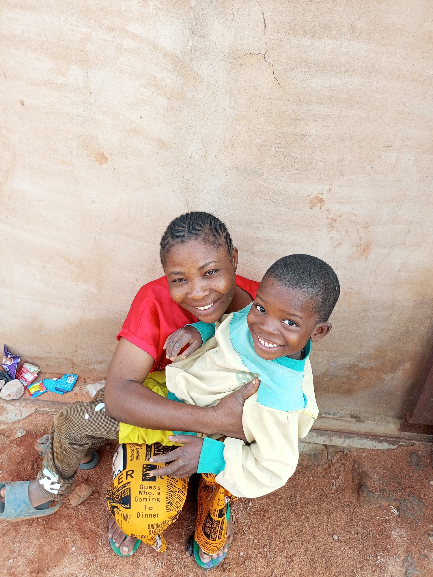 Braided hair, bundled child, warm smile by a tan wall