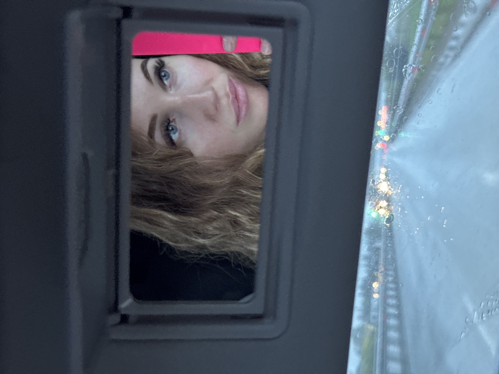 Woman uses car mirror with pink object in wet Russian town