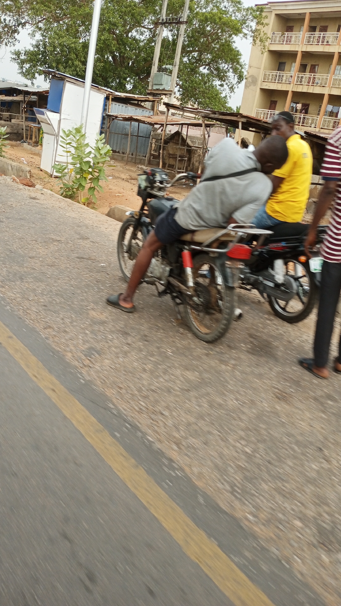 Three people gather with motorcycles on Adankolo road