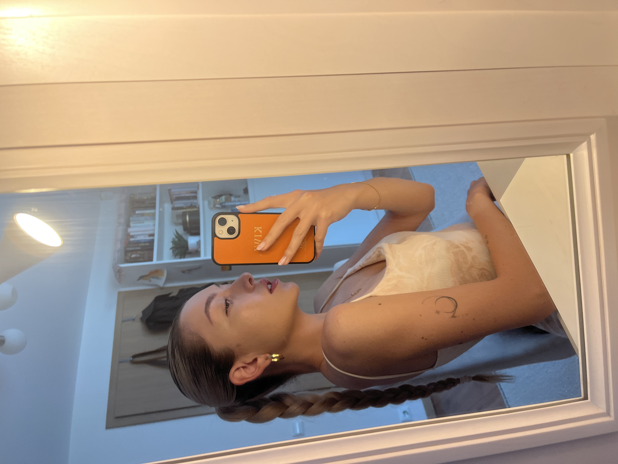 Woman takes multiple mirror selfies with personalized orange phone case