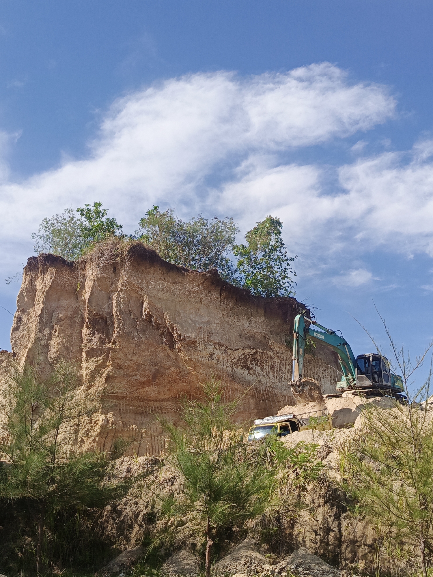 Excavator cuts into cliff face at Lhokseumawe construction site