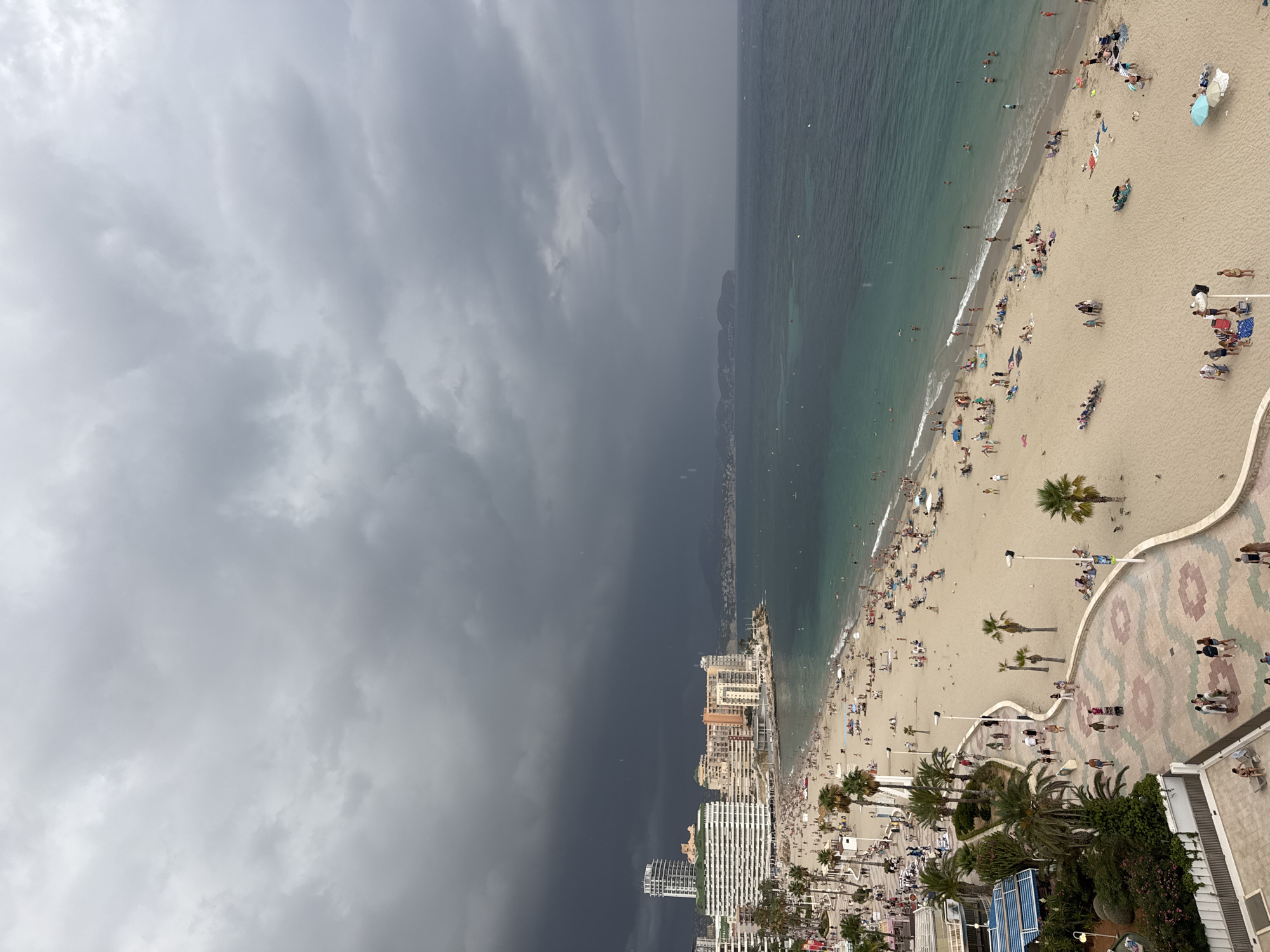 Storm front moves in over packed Calp beach, Penyal d'Ifac backdrop