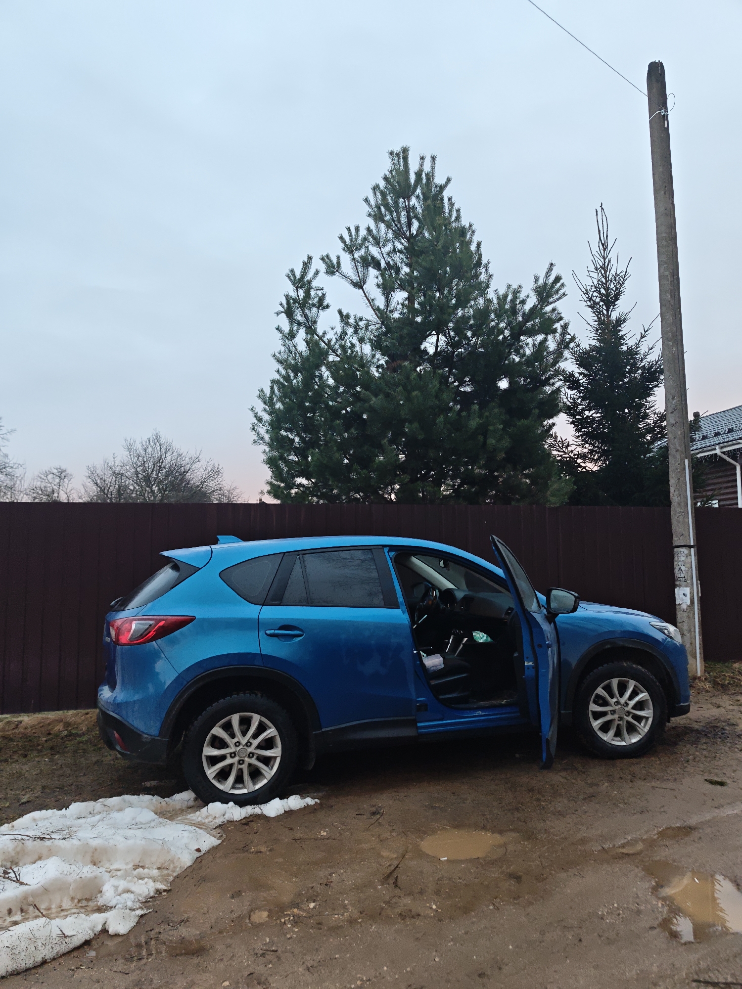 Person takes selfies by blue Mazda on muddy Russian village roads