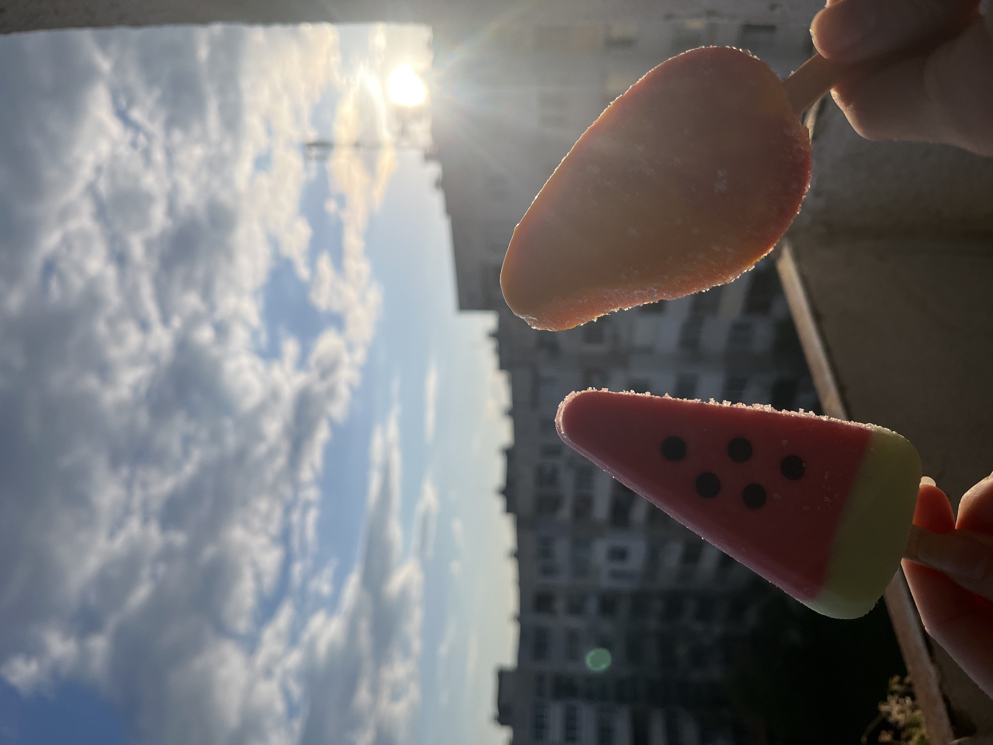 Person enjoys watermelon popsicles under sunny Sofia sky