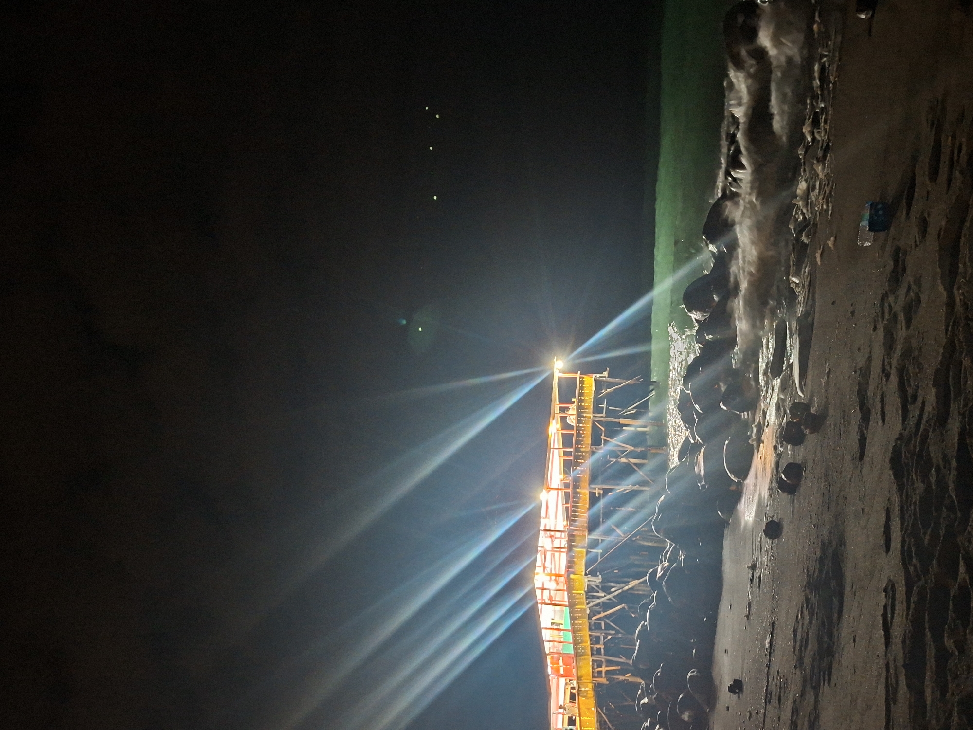 Illuminated pier captures attention during nighttime beach activity in Lhokseumawe