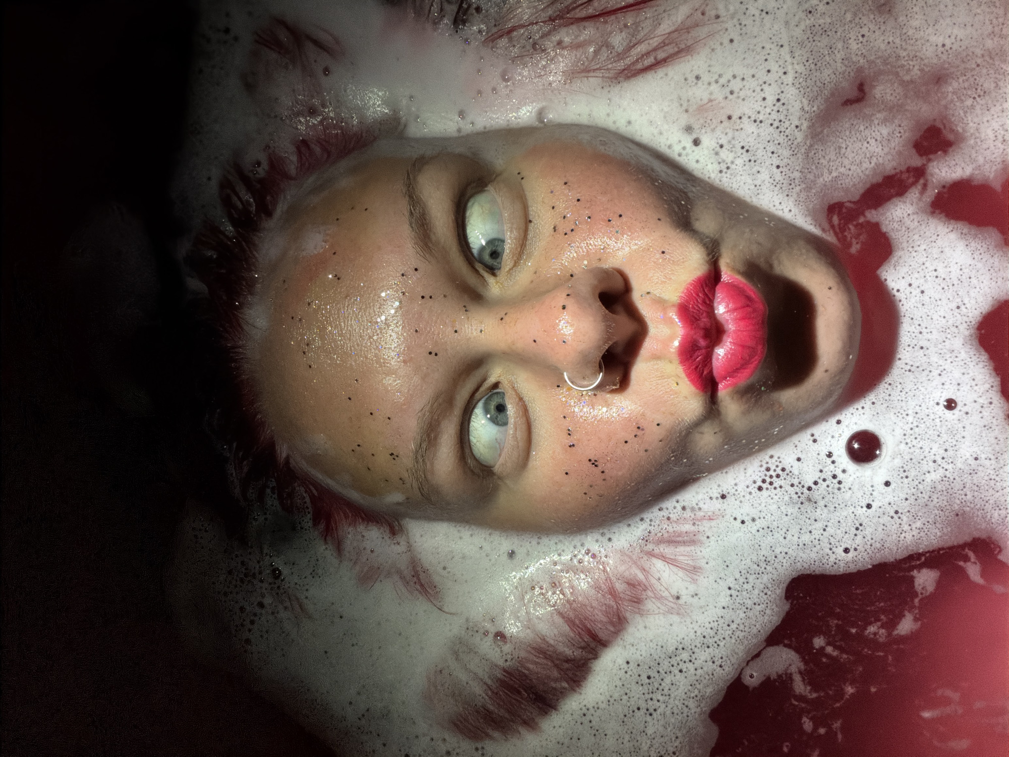 Person photographed partially submerged in red-tinted foamy water