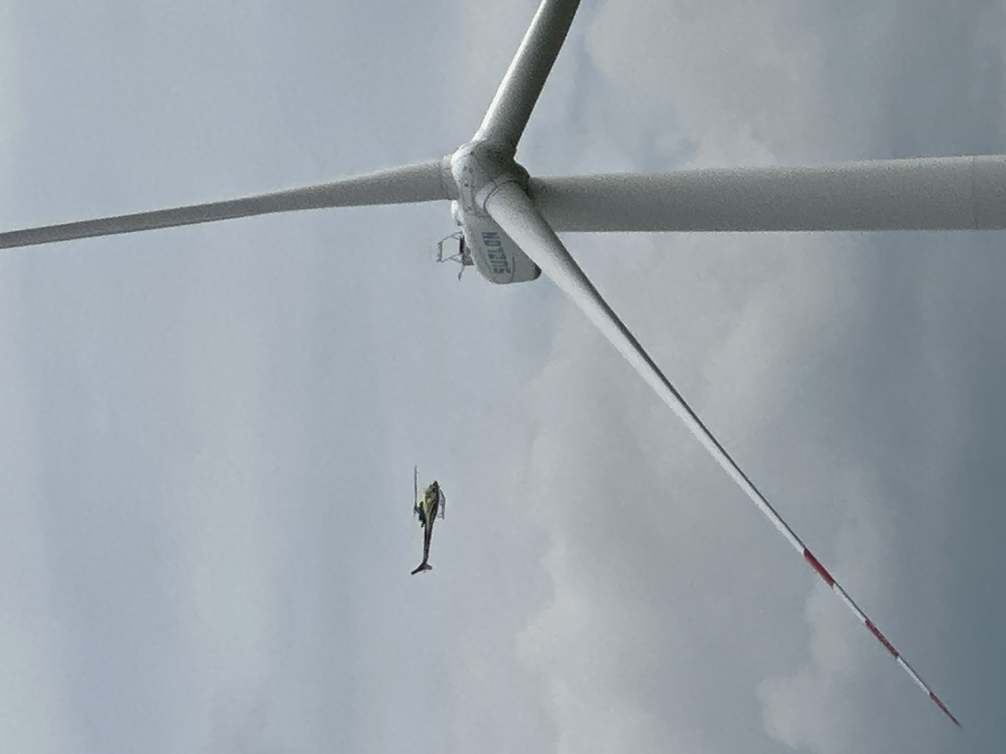 Yellow helicopter flies past wind turbine and comms tower in rural Ukraine