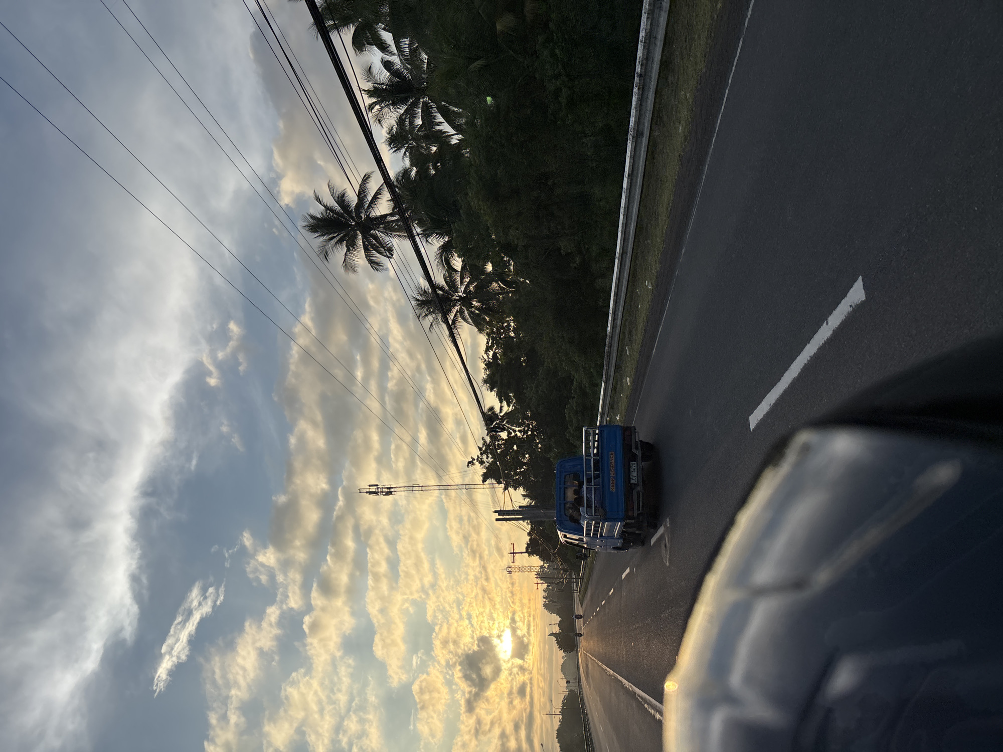 Blue pickup truck travels Philippine highway at sunset
