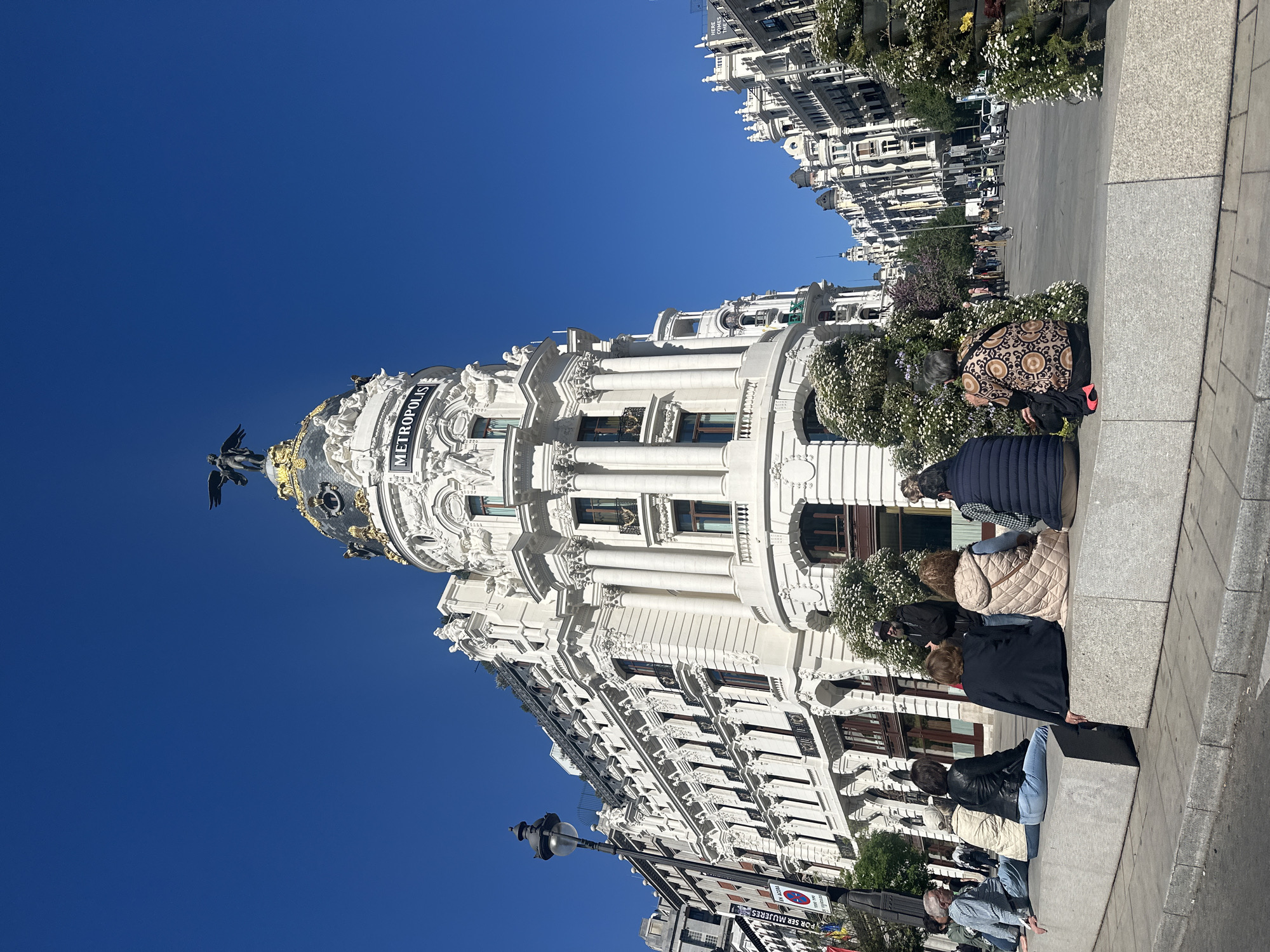 People gather near Madrid's historic Metropolis Building under clear skies