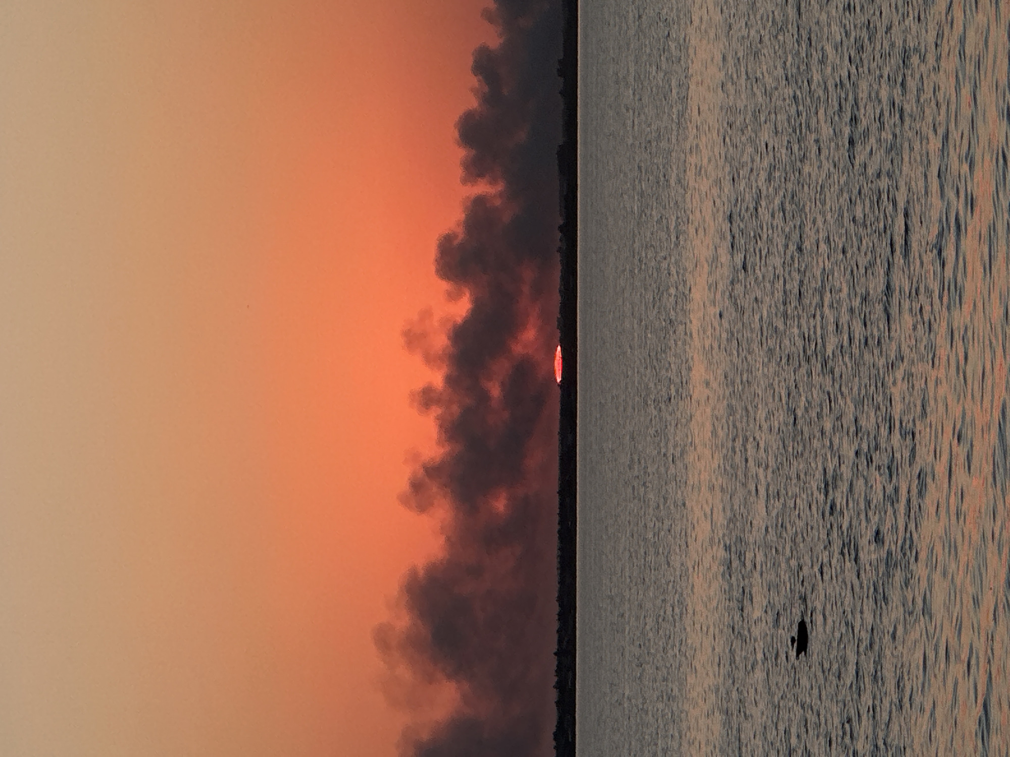 Dark smoke rises against a fiery sunset over Kokshetau water