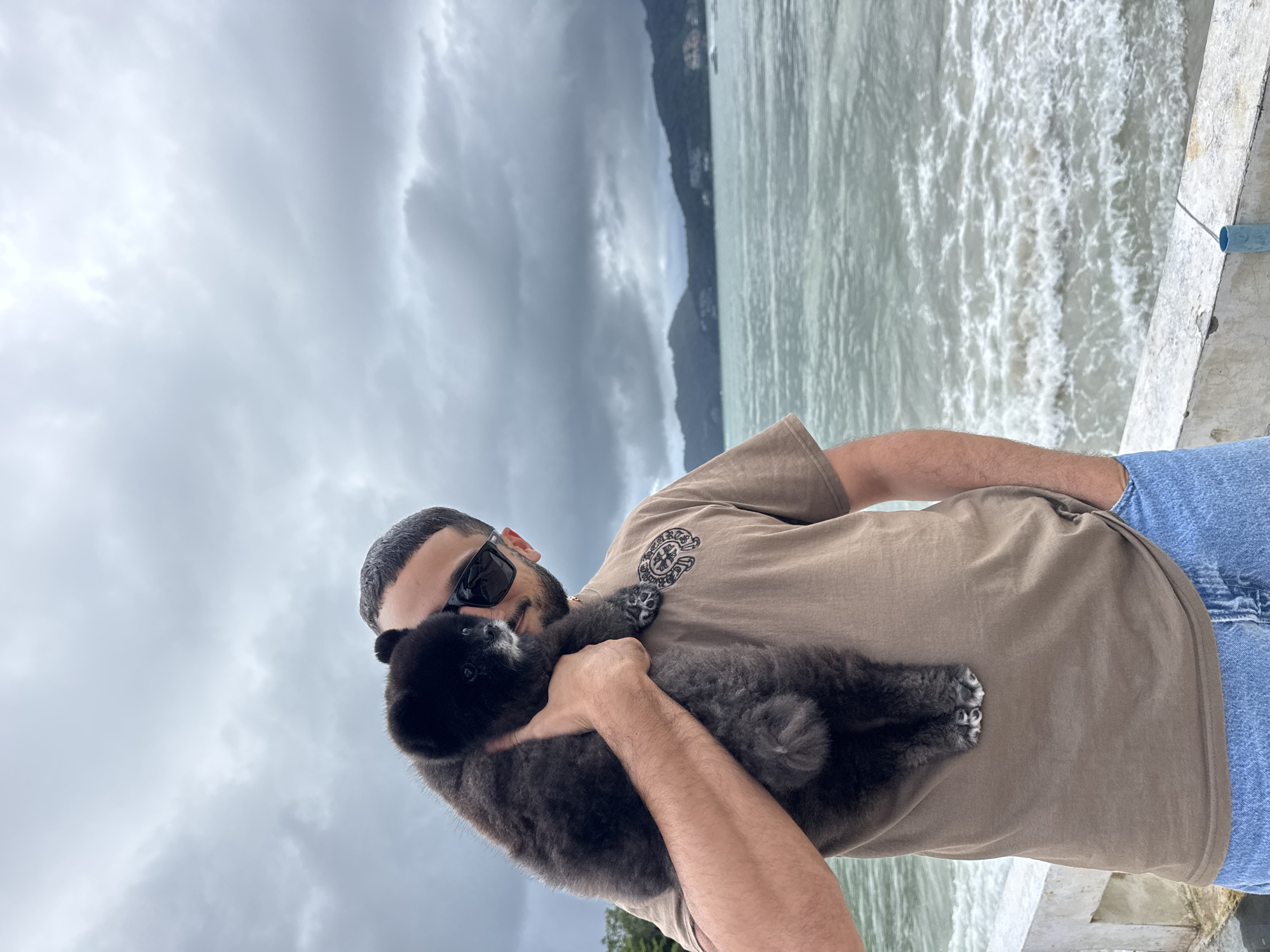 Couple with black dog tours Thai coast under cloudy skies
