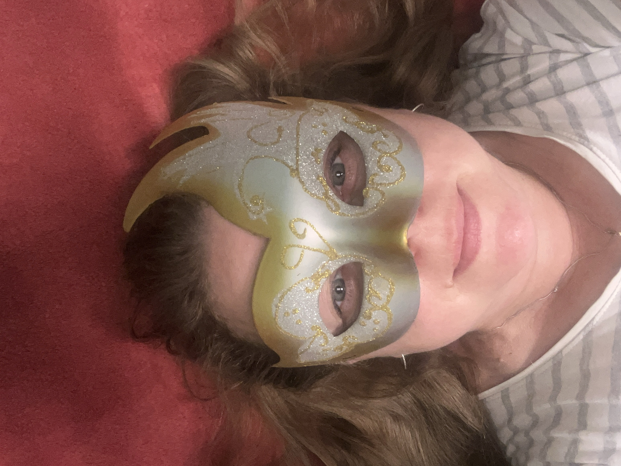 Masked portrait lying down against a vivid red backdrop.