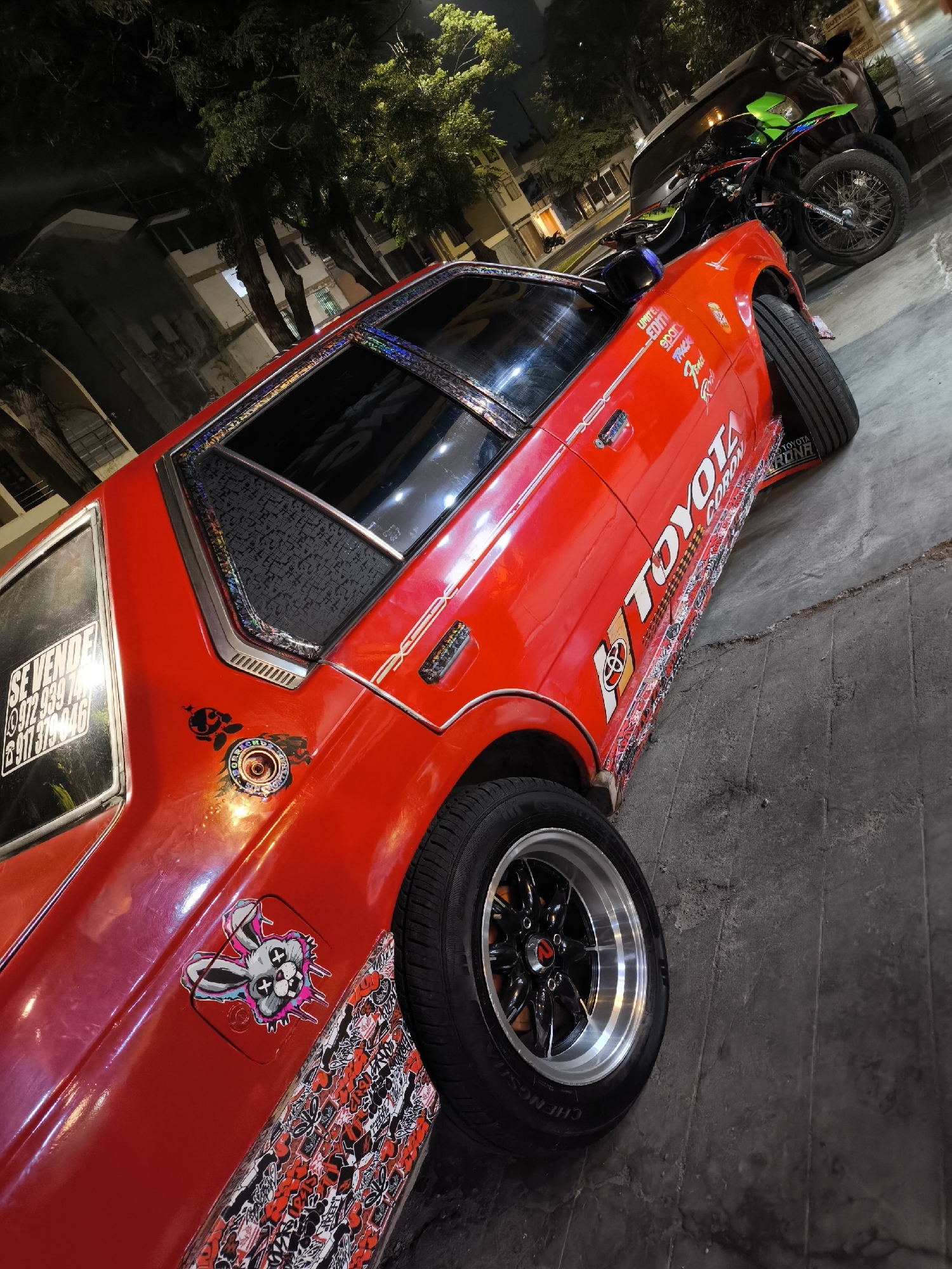 Modified red Toyota with for-sale sign parked at night