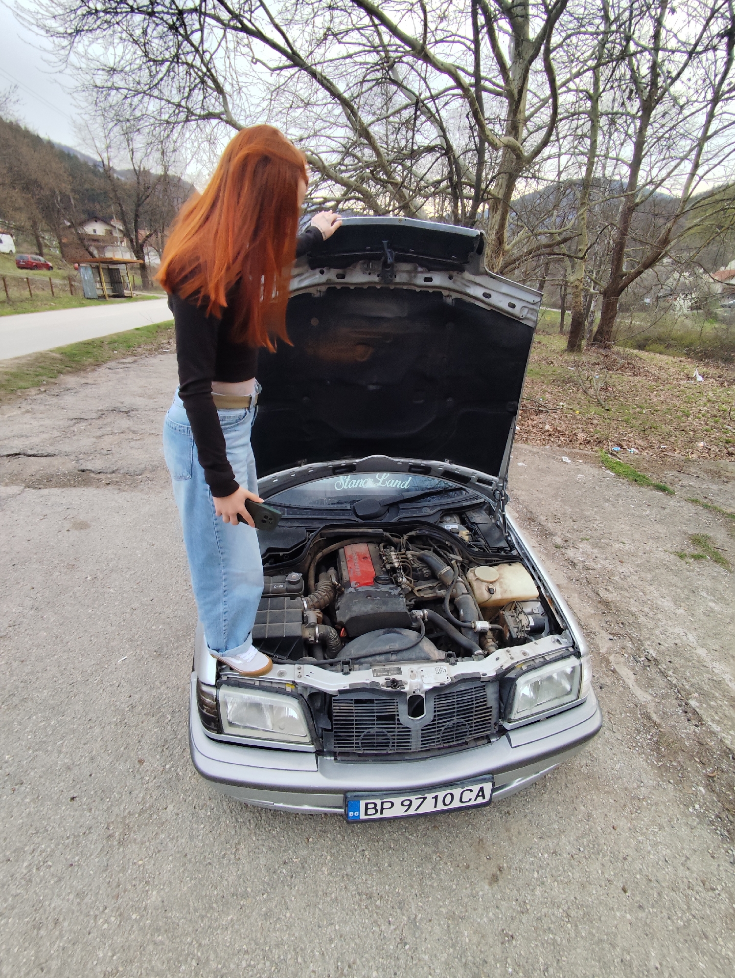 Woman inspects car engine from hood in Bulgarian mountains