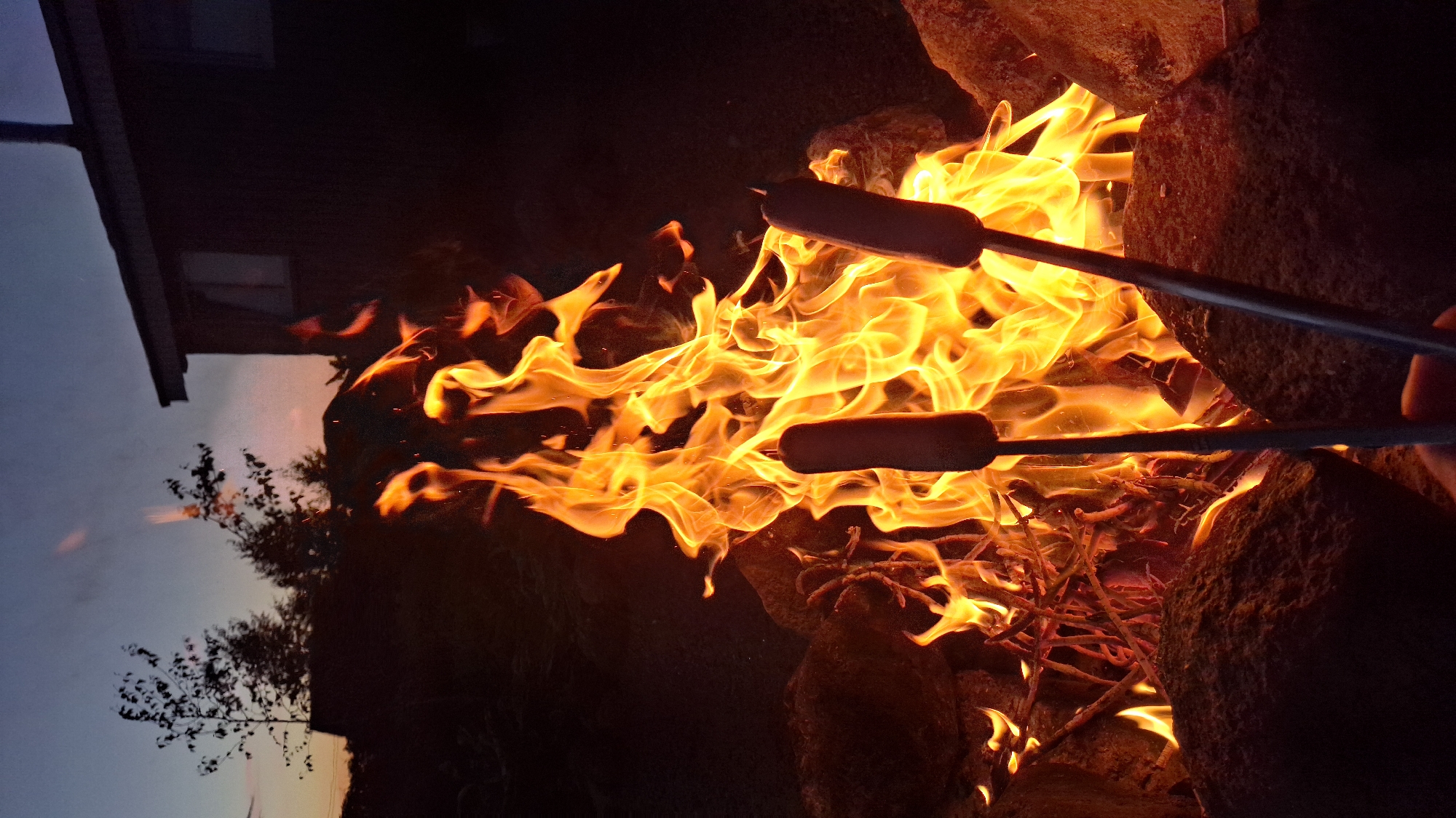 Backyard bonfire and hot dogs over a stone fire pit at dusk