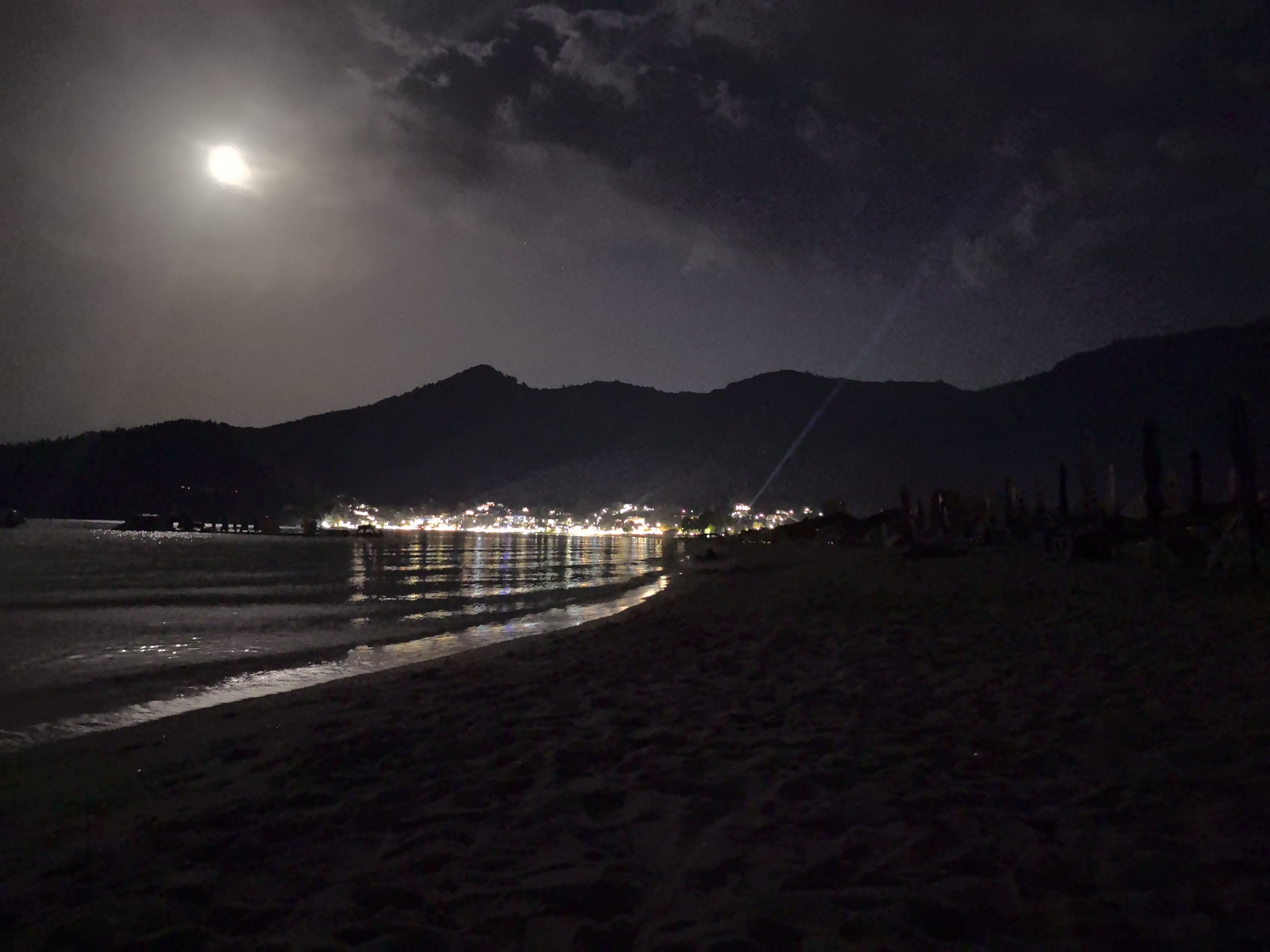 Moonlit night at Golden Beach with mountain silhouette and distant town lights