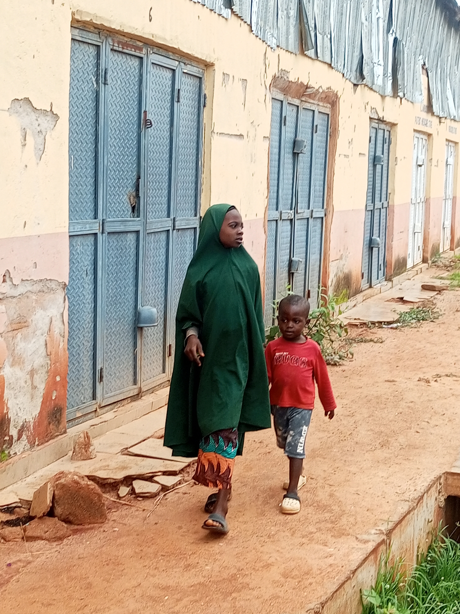 Children and adult walking a dirt path beside a building