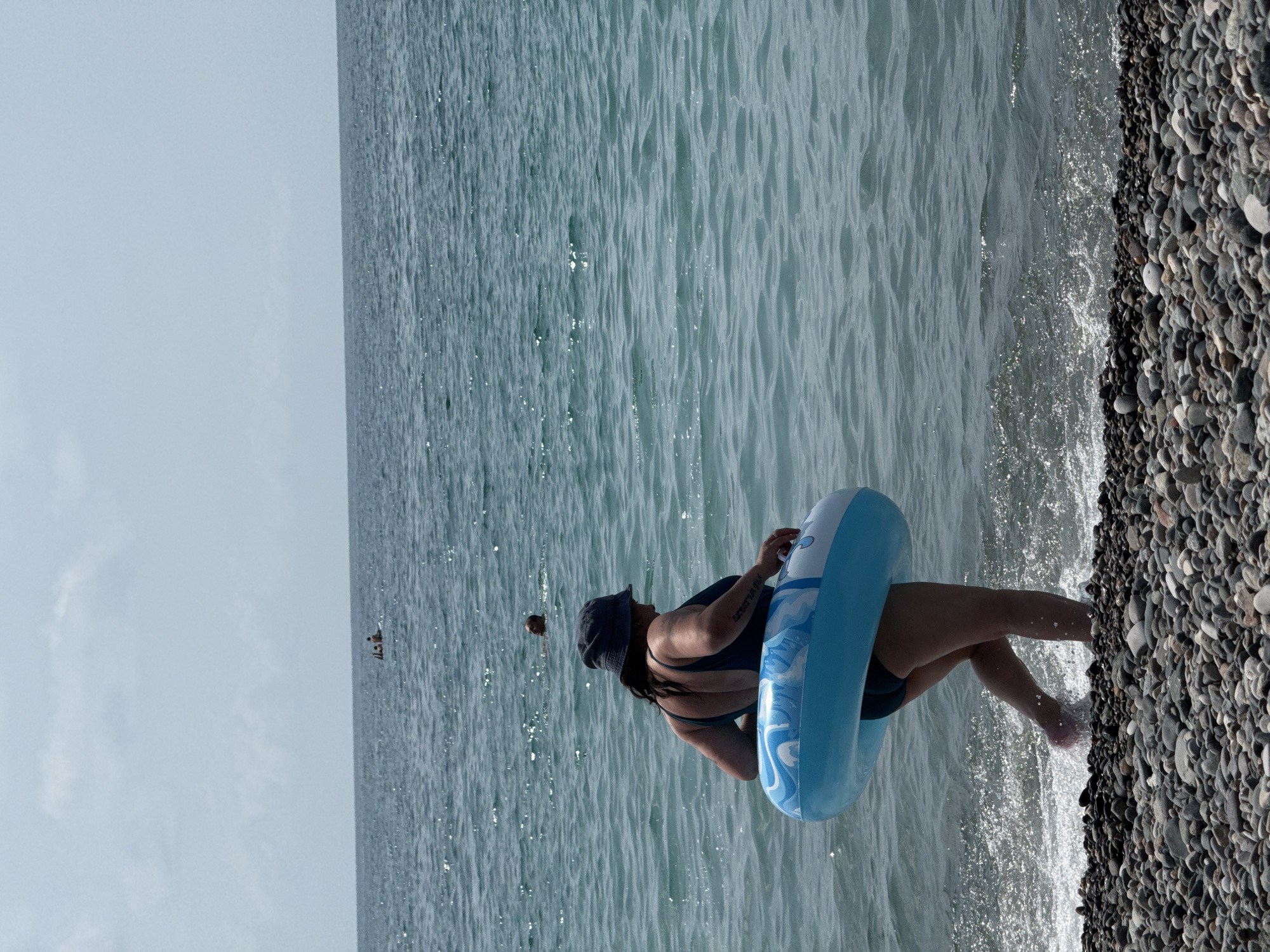 Busy resort beach day with swimmers, sunbathers, and a hilltop cross